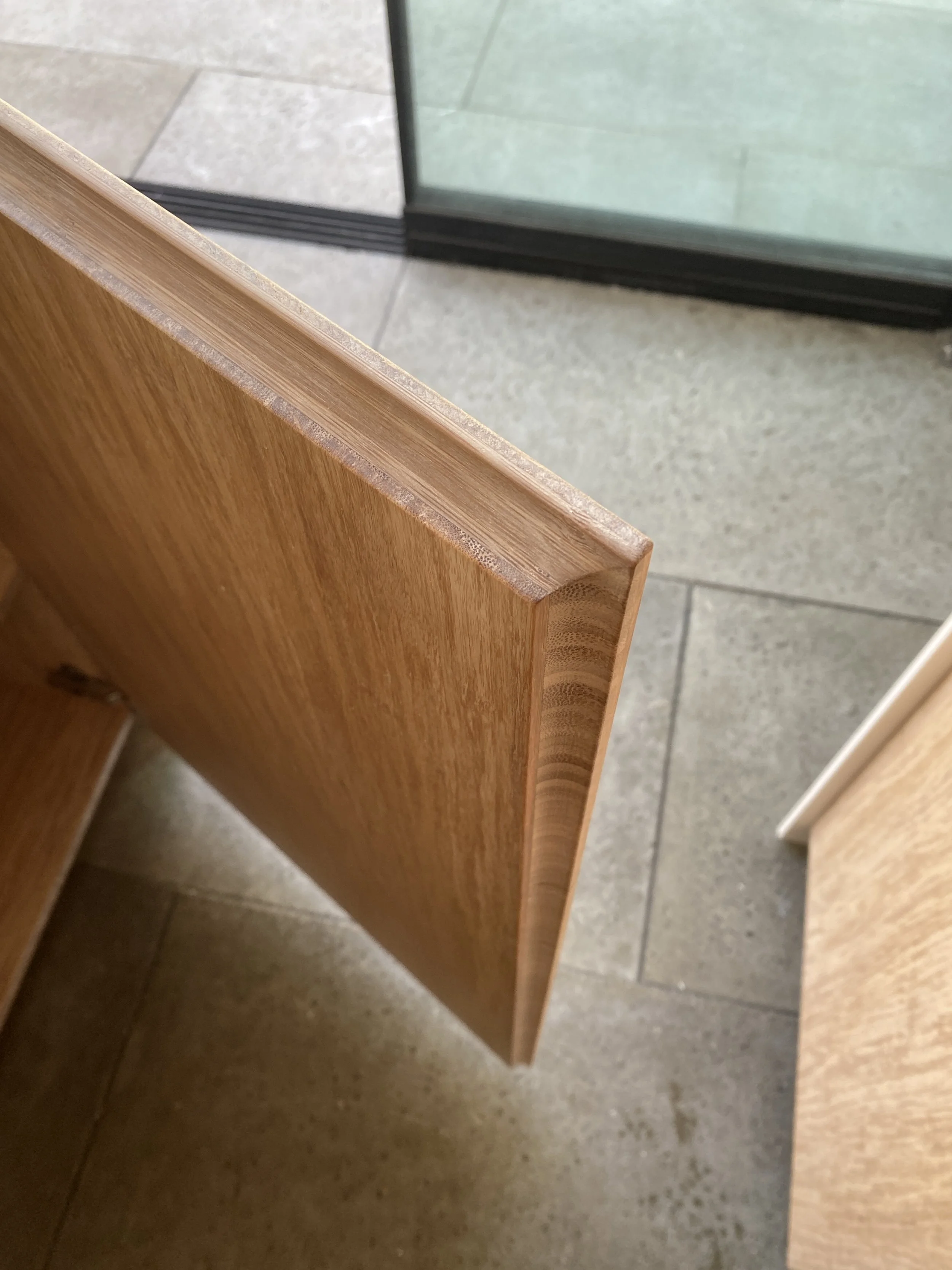 Close-up van de rand van een houten meubelstuk met een glazen deur op een tegelvloer.