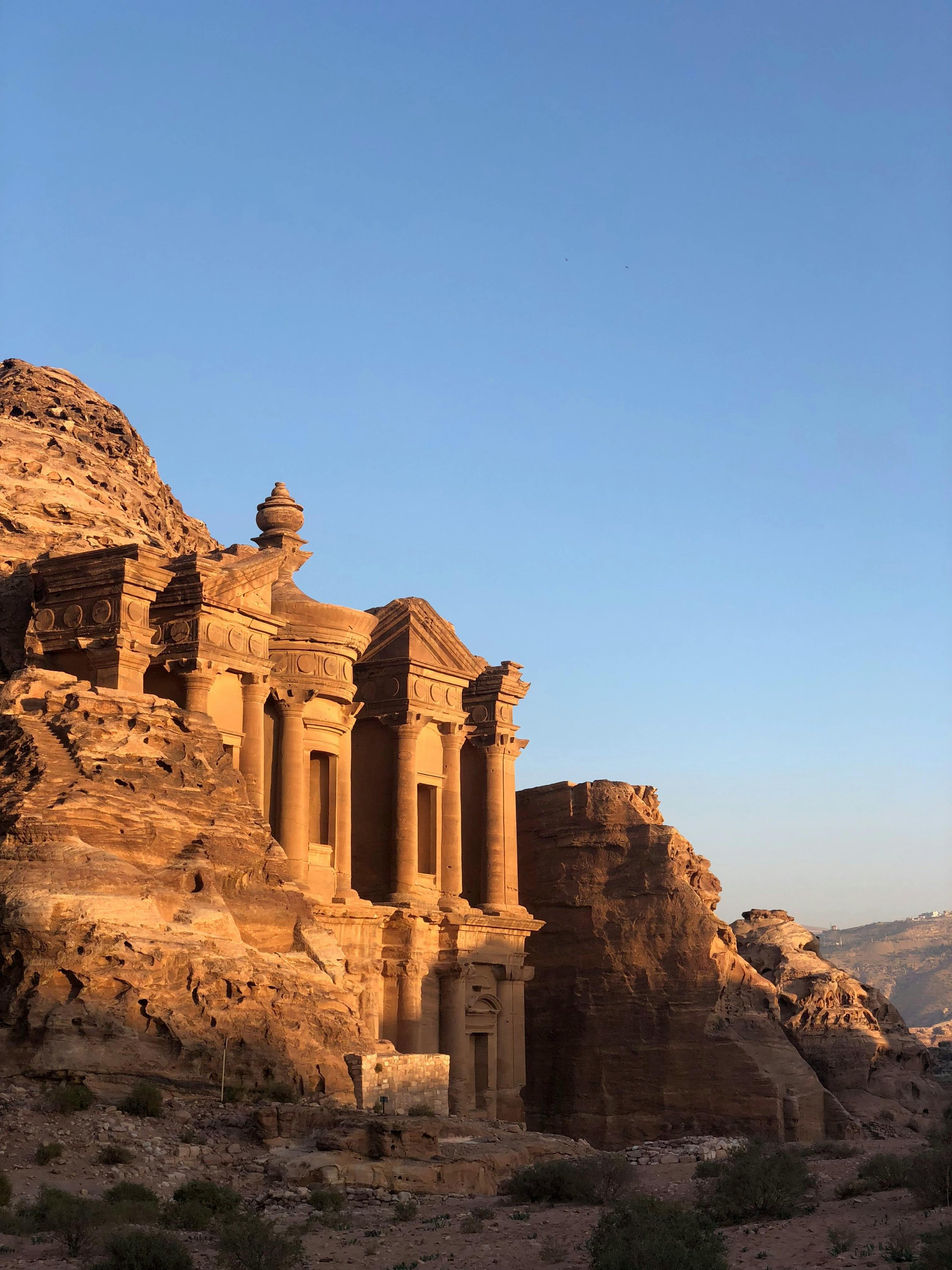 Ancient rock-cut city with grand facades, columns, and intricate carvings, illuminated by warm sunlight against a clear blue sky.