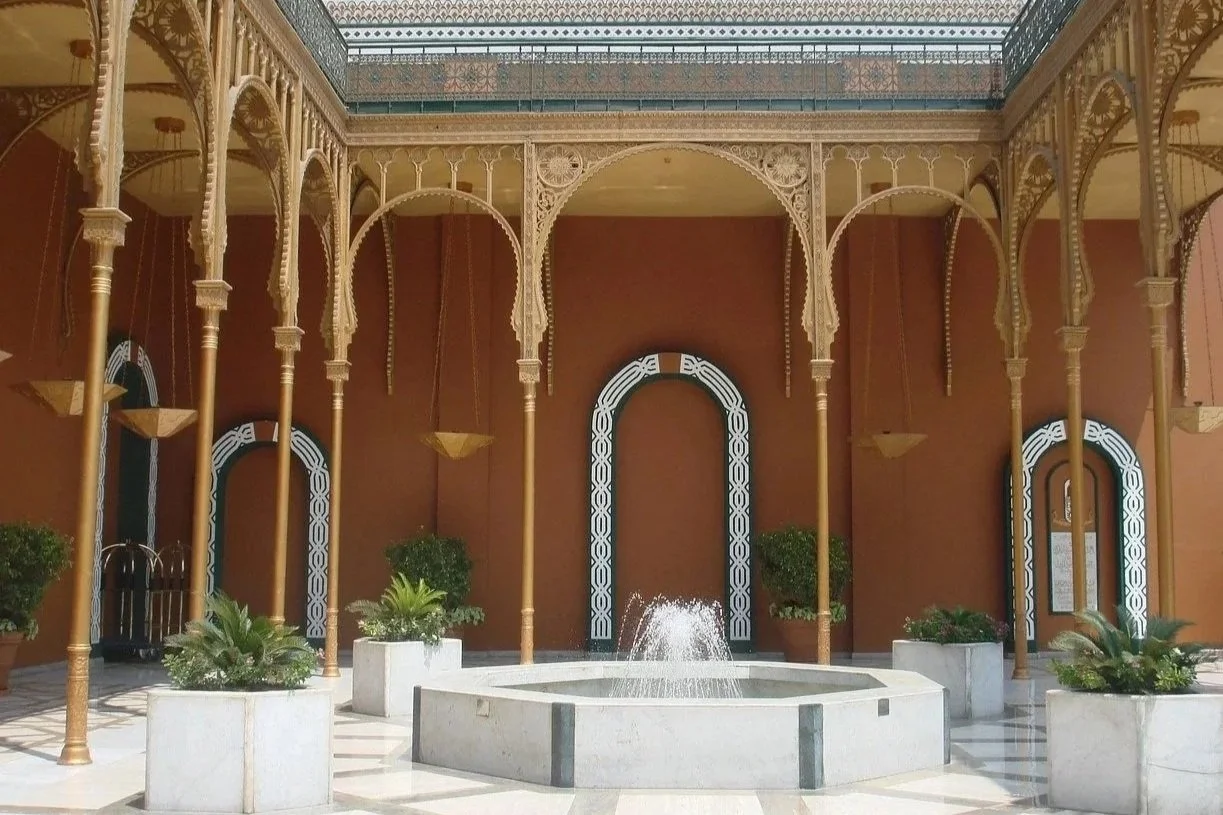 Interior courtyard with ornate arches, gold columns, a central fountain, and potted plants.