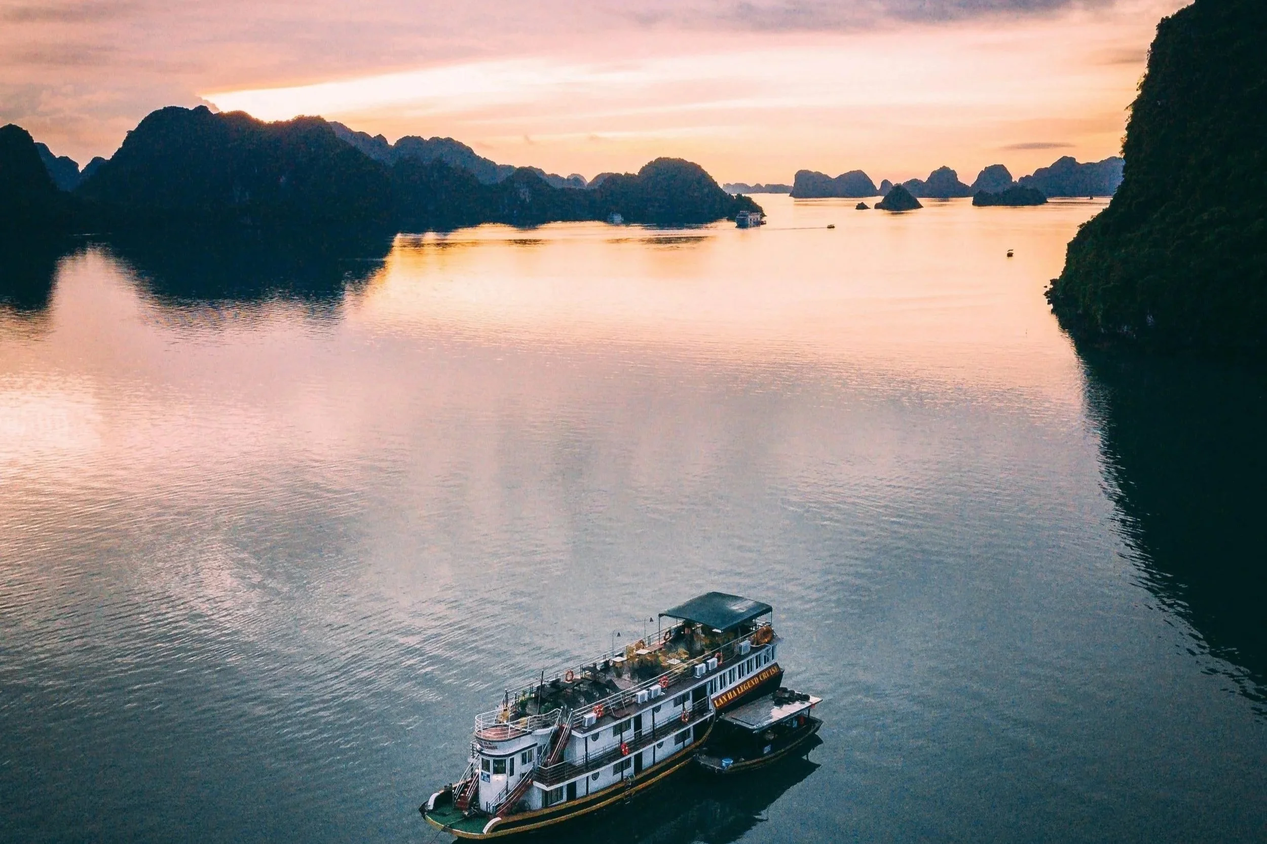 A boat floating on calm waters during a sunset with rocky islands and hills in the background