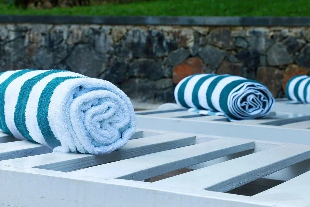 Rolled-up striped towels placed on a white wooden lounge chair outdoors.
