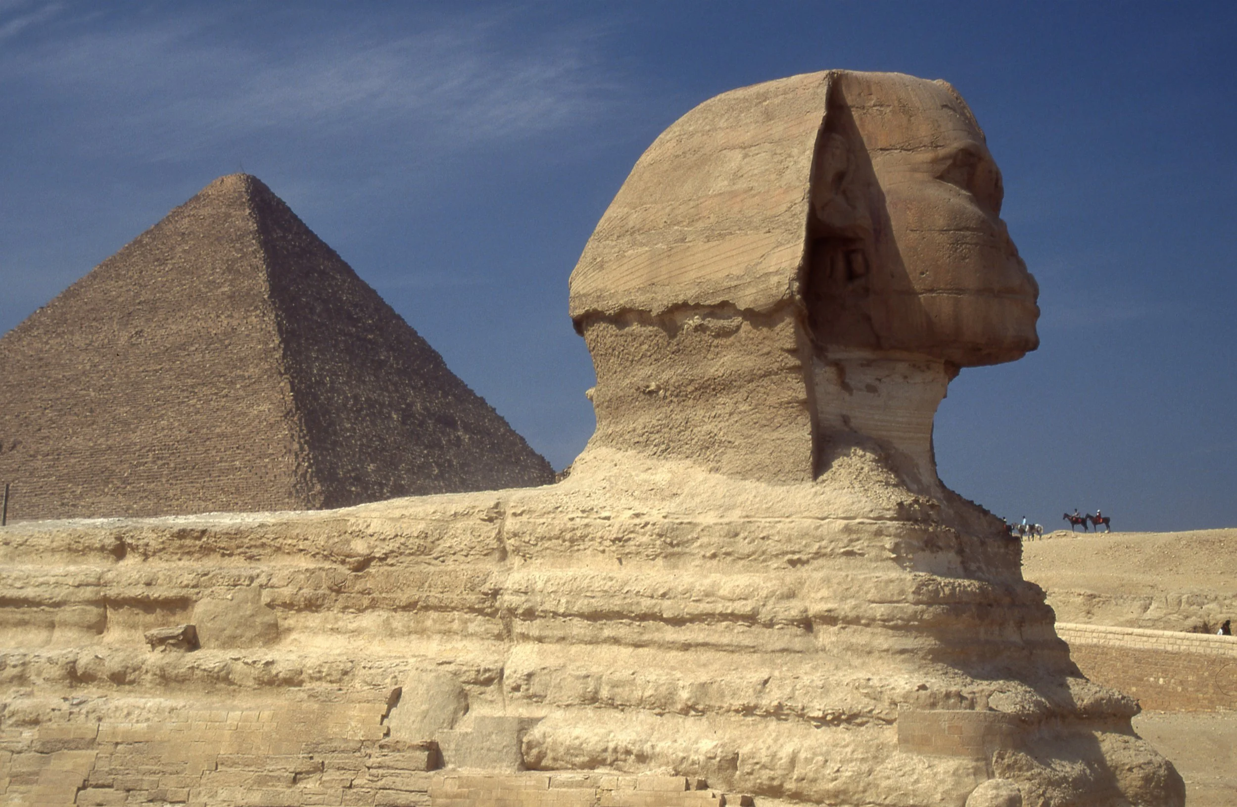 Close-up of the Great Sphinx of Giza with the Pyramid of Khafre in the background, under a clear blue sky.