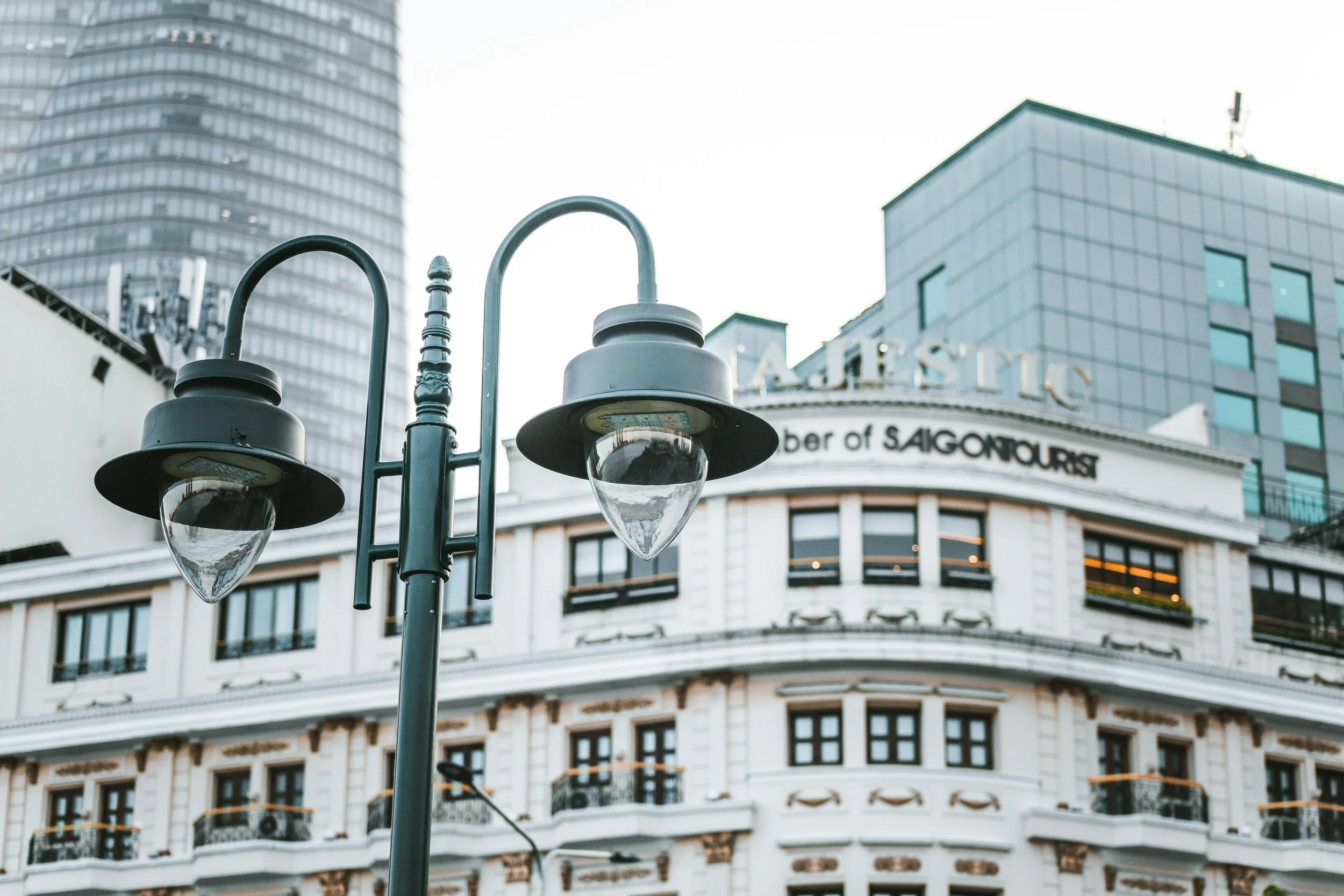 Street lamp with two fixtures in front of a historic building with rounded facade and the words 'Number of SAIGONTOURIST' on top, in an urban cityscape.
