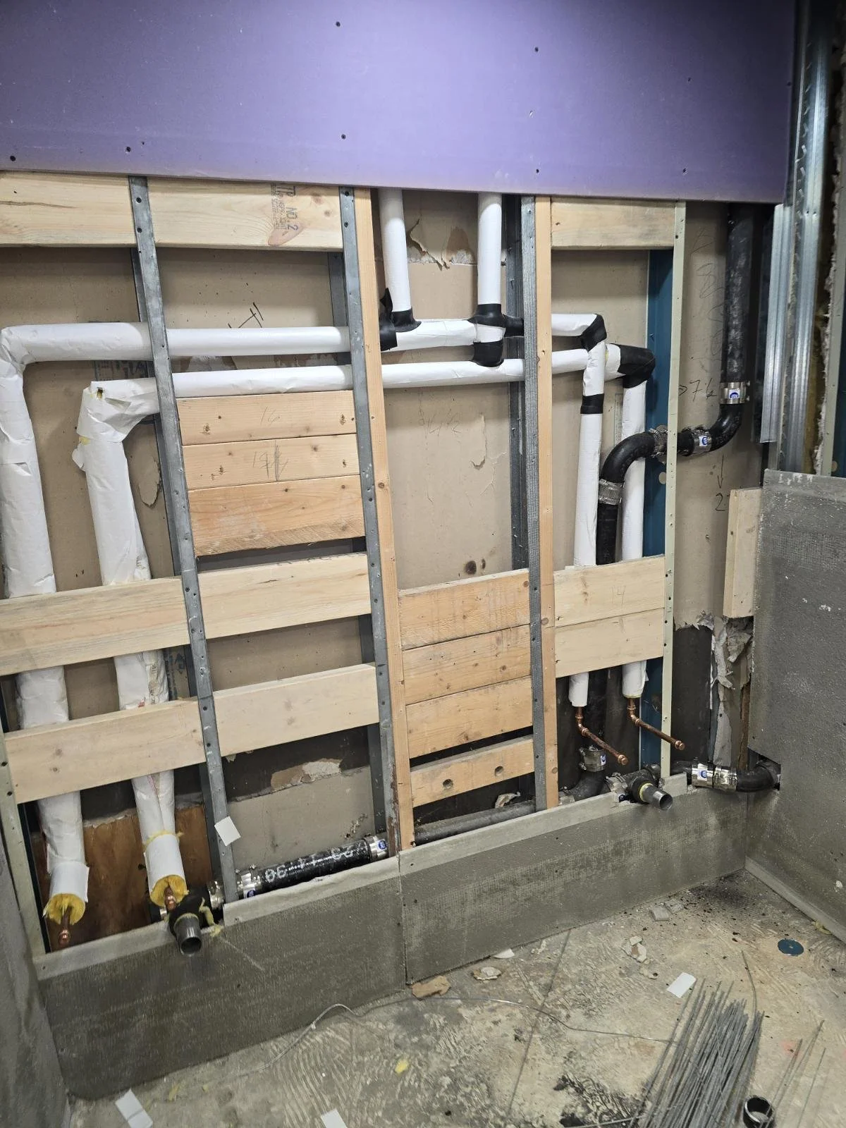 Construction of a bathroom with exposed plumbing, framed wall with wood and metal studs, and pipes for water supply and drainage.