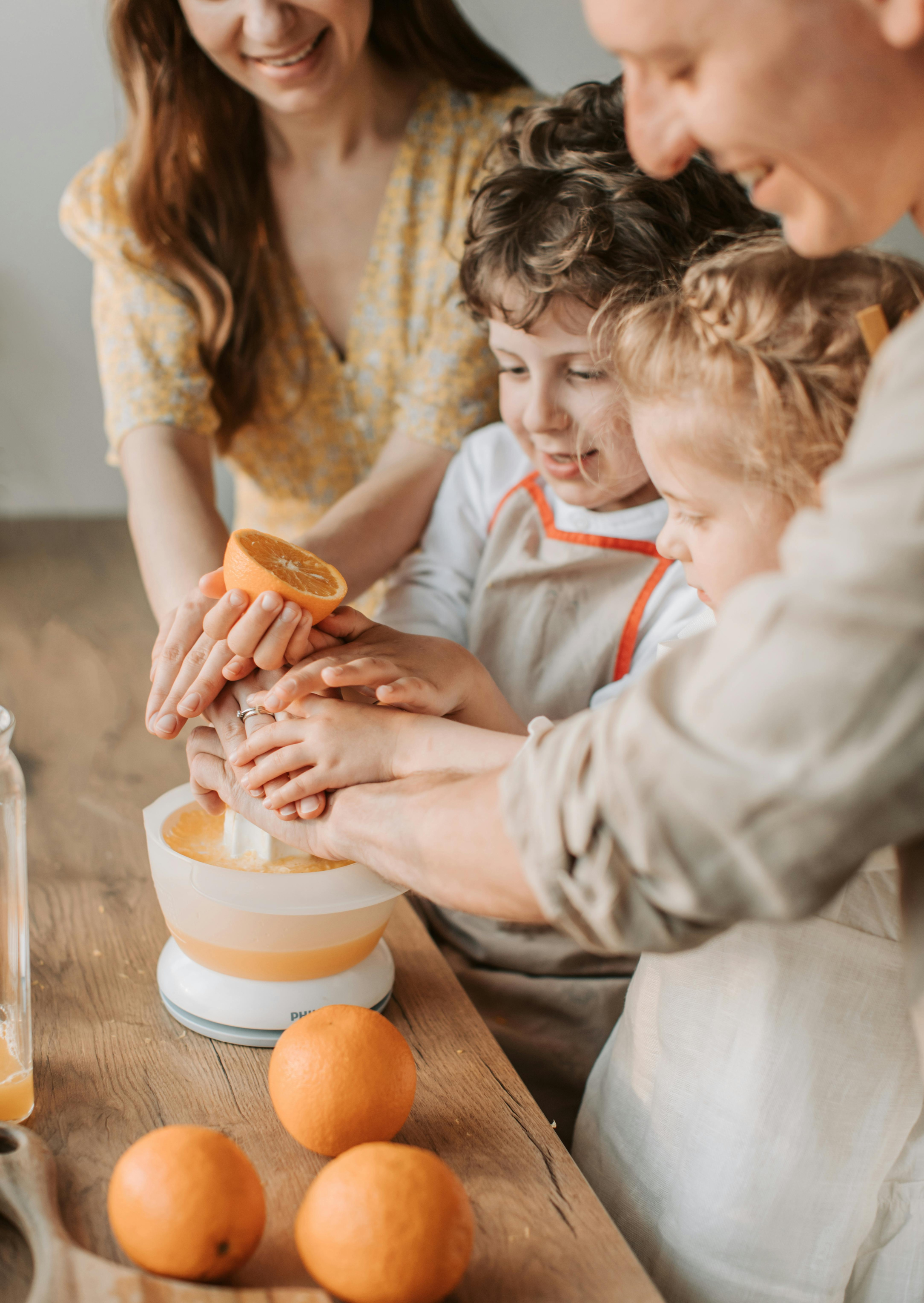 Una familia preparando jugo de naranja en la cocina, con naranjas sobre la mesa.