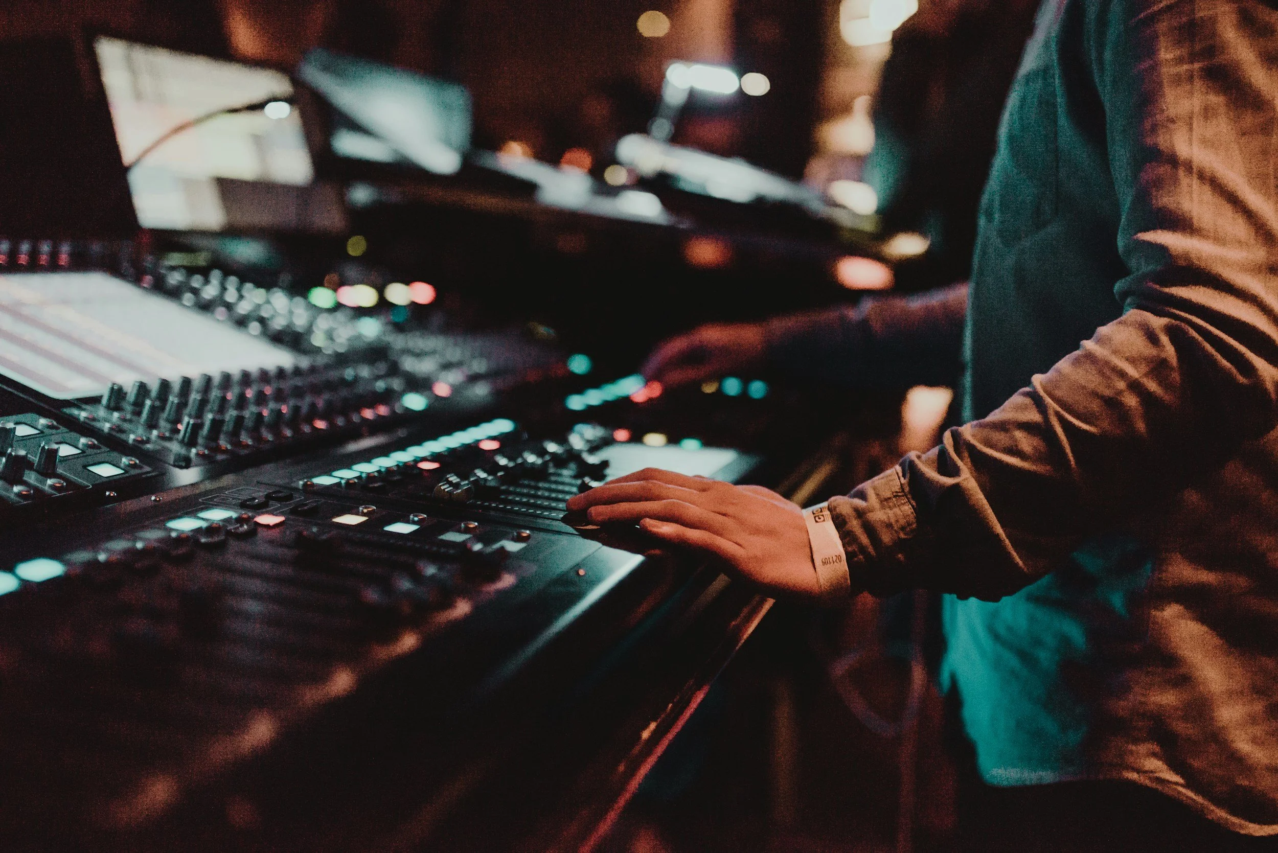 A DJ performing with hands on a professional DJ mixer and turntable in a dimly lit setting.