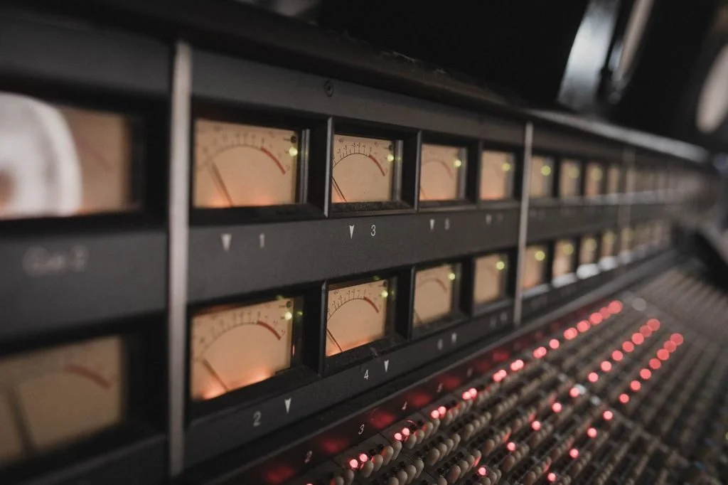 A professional audio mixing console with illuminated meters and numerous red-lit control lights.