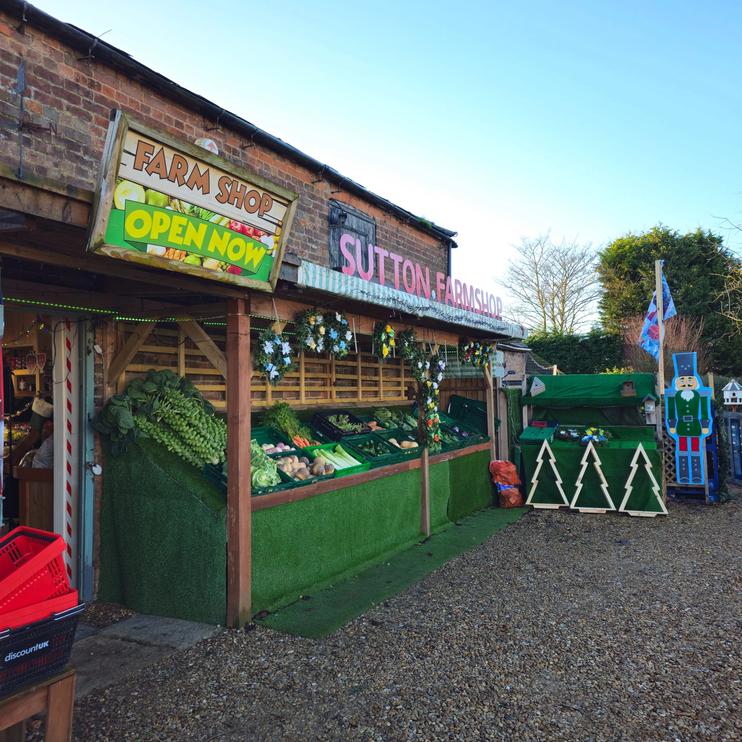 The heart of Sutton Farm Shop, captured in winter light. Wreaths and greenery frame the storefront, inviting customers into a world of fresh produce and festive charm. The rustic textures of brick, timber, and greenery tell a story of heritage and lo