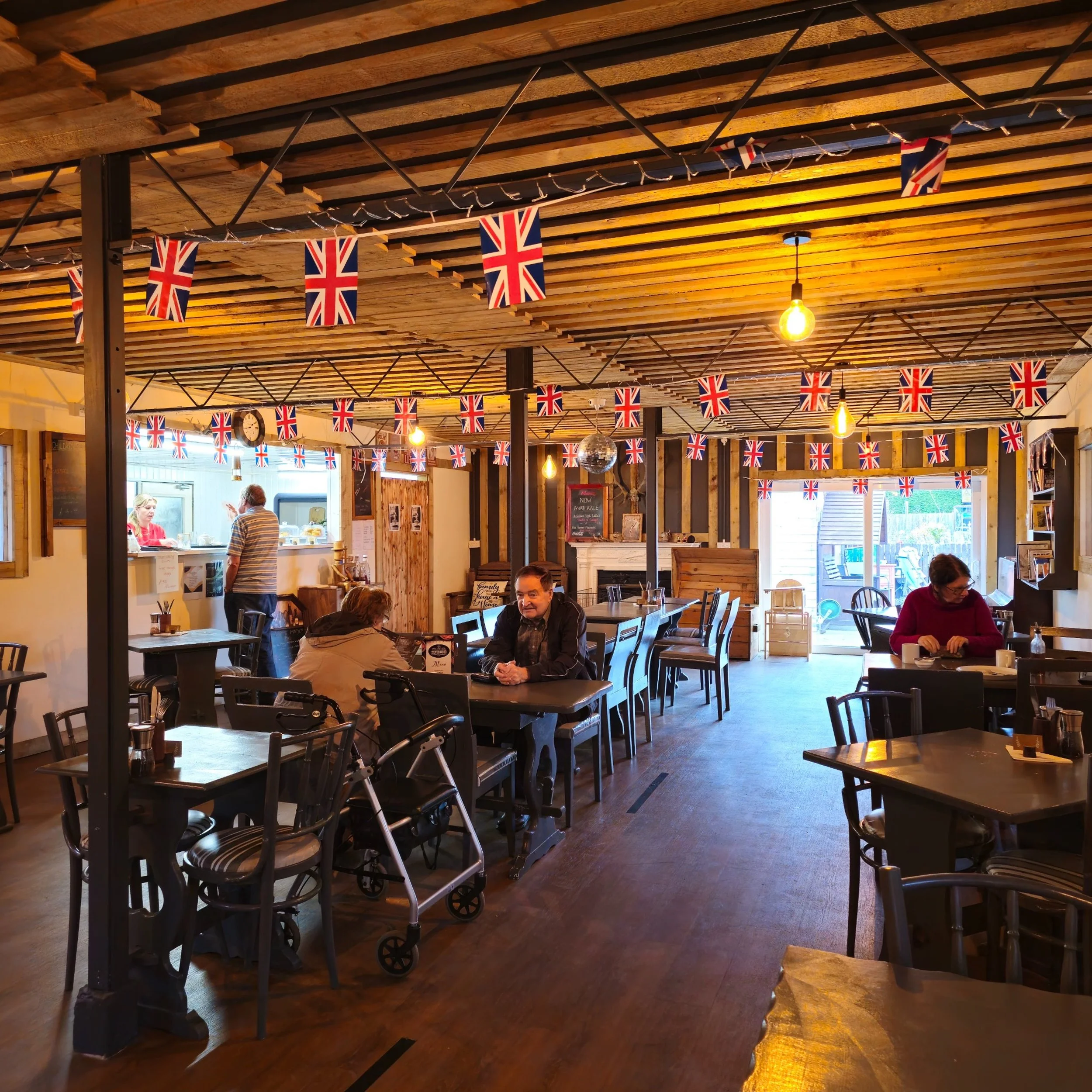 The welcoming interior of Silverwood Garden Centre & Café, decorated with Union flag bunting and warm lighting. This photo captures the cosy, community-centred atmosphere, ideal for promoting dine-in comfort and the café’s friendly, homely environmen