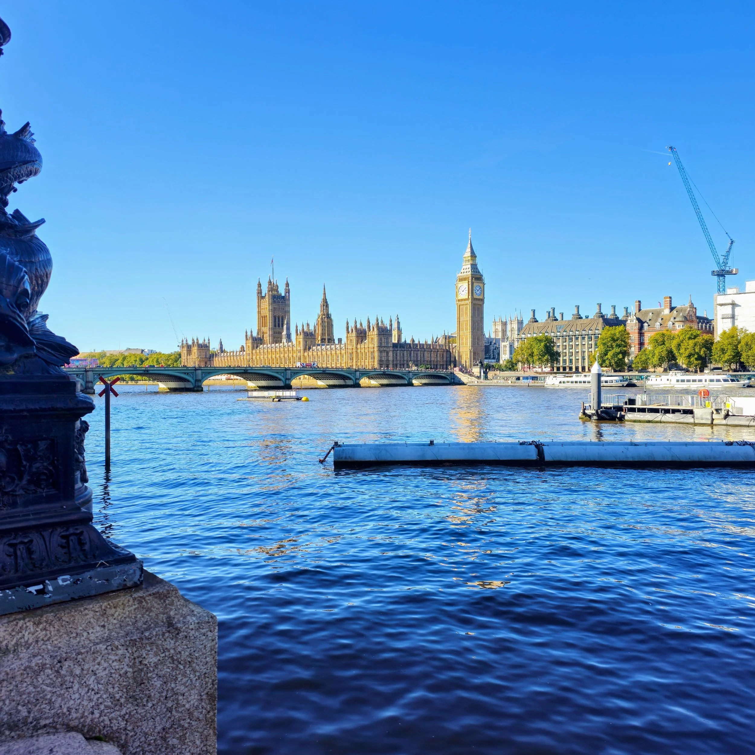 Stunning riverside view of the Houses of Parliament and Big Ben in London, with Westminster Bridge reflecting over the River Thames on a bright sunny day—perfect for travel, tourism, and UK destination websites.