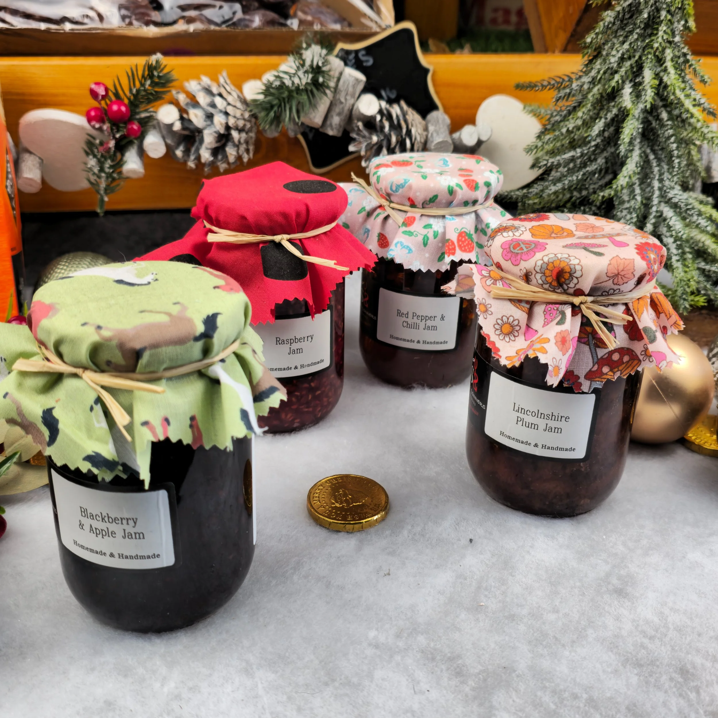 Four jars of homemade jam stand like a tribute to heritage and care. Their fabric lids, tied with twine, echo tradition while each label proudly tells its story. The image is a study in warmth and craftsmanship—proof that even the smallest details ca