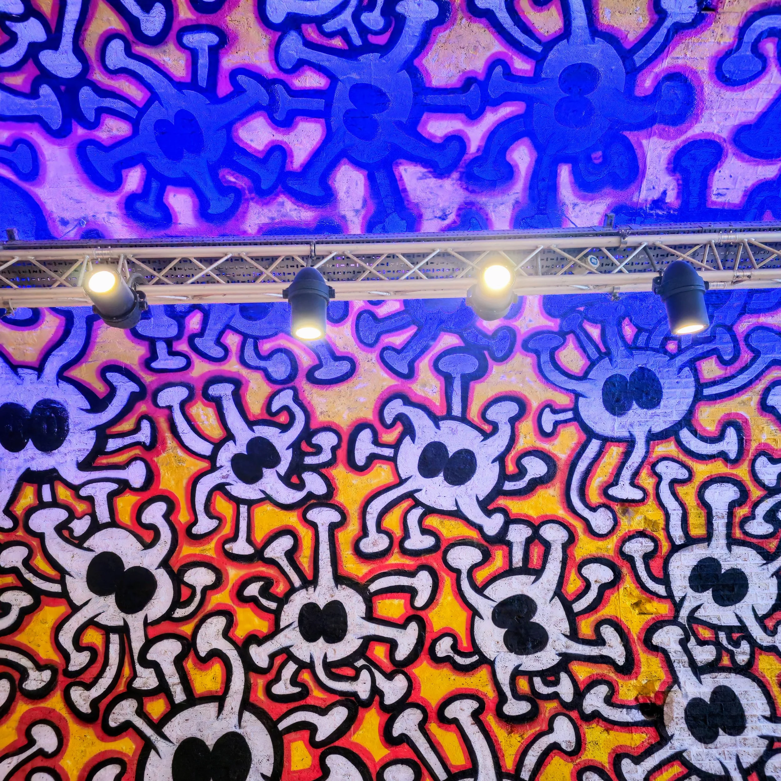 A vibrant street-art ceiling filled with bold cartoon-style characters illuminated by overhead stage lighting. This photograph showcases dynamic shapes, neon colours, and urban creativity, capturing the energy of contemporary graffiti culture. Perfec