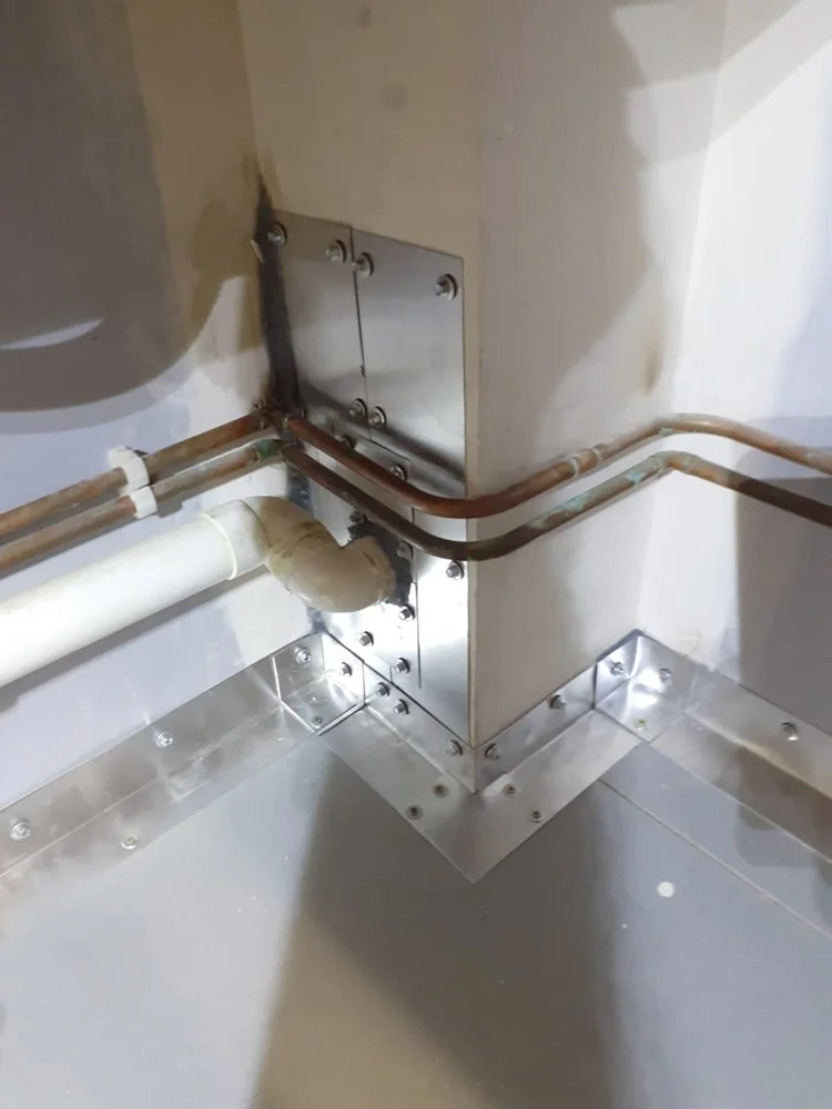 Close-up of a corner in a building with electrical and plumbing installations, including copper pipes, a pipe with insulation, and metal brackets and plates securing the fixtures.