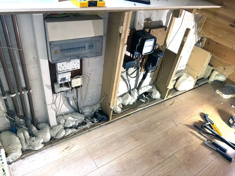 Electrical wiring and circuit breaker panel setup in a basement or workshop with tools on the floor.