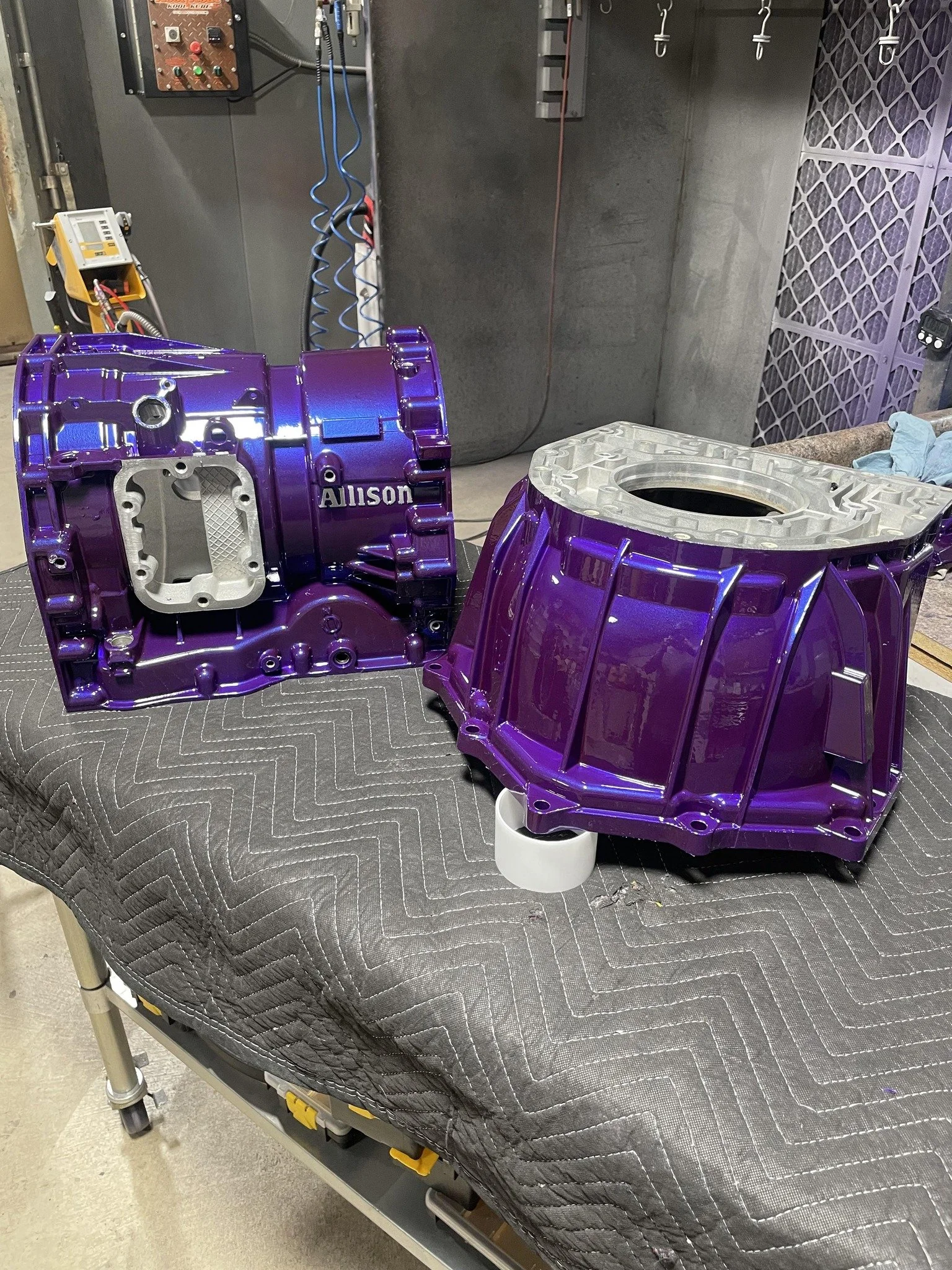 A purple automotive transmission case and a purple differential housing on an inspection pad, in a workshop.