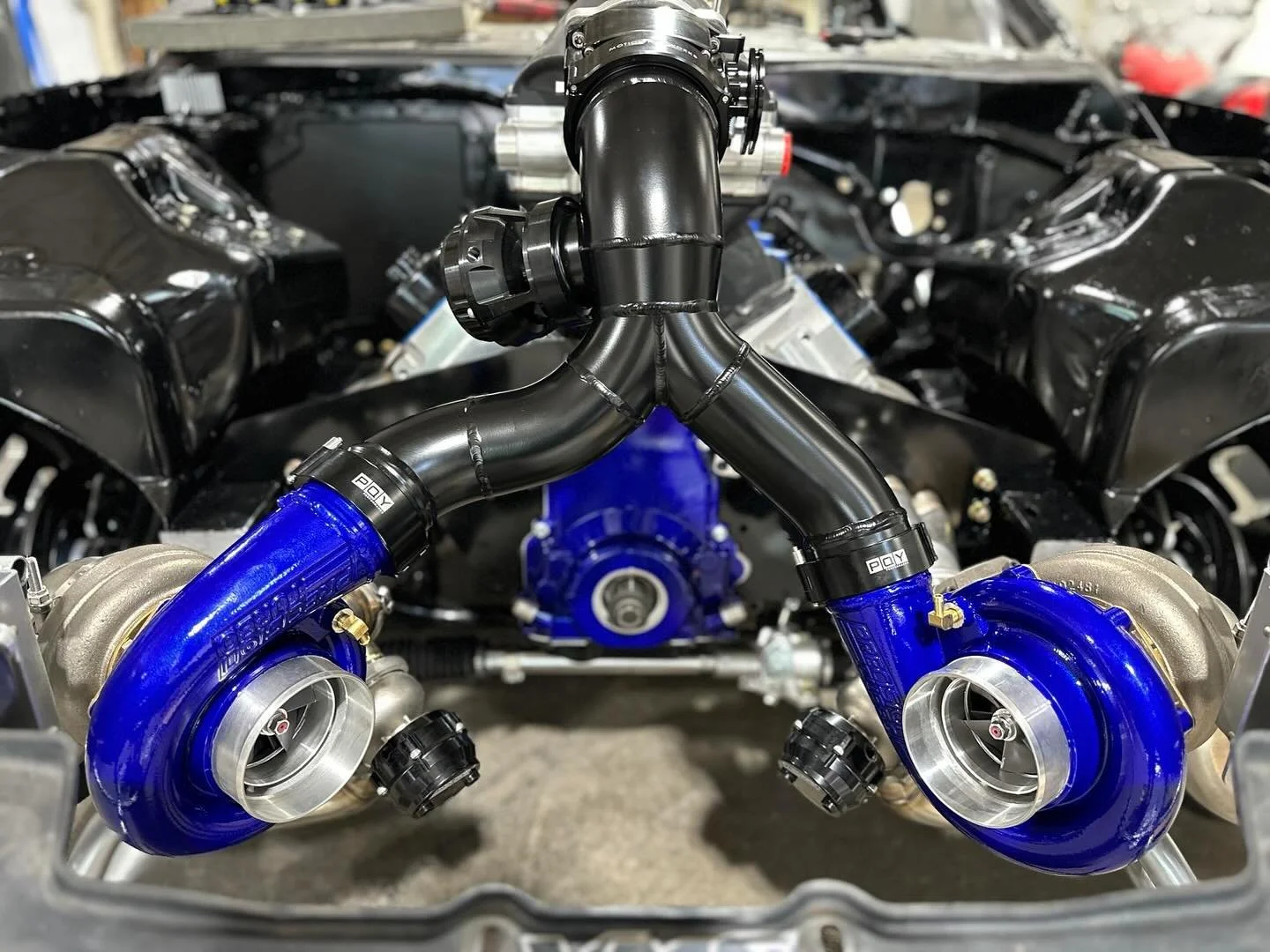 A close-up view of a car engine with a black intake pipe and blue turbochargers, inside a car's engine bay.