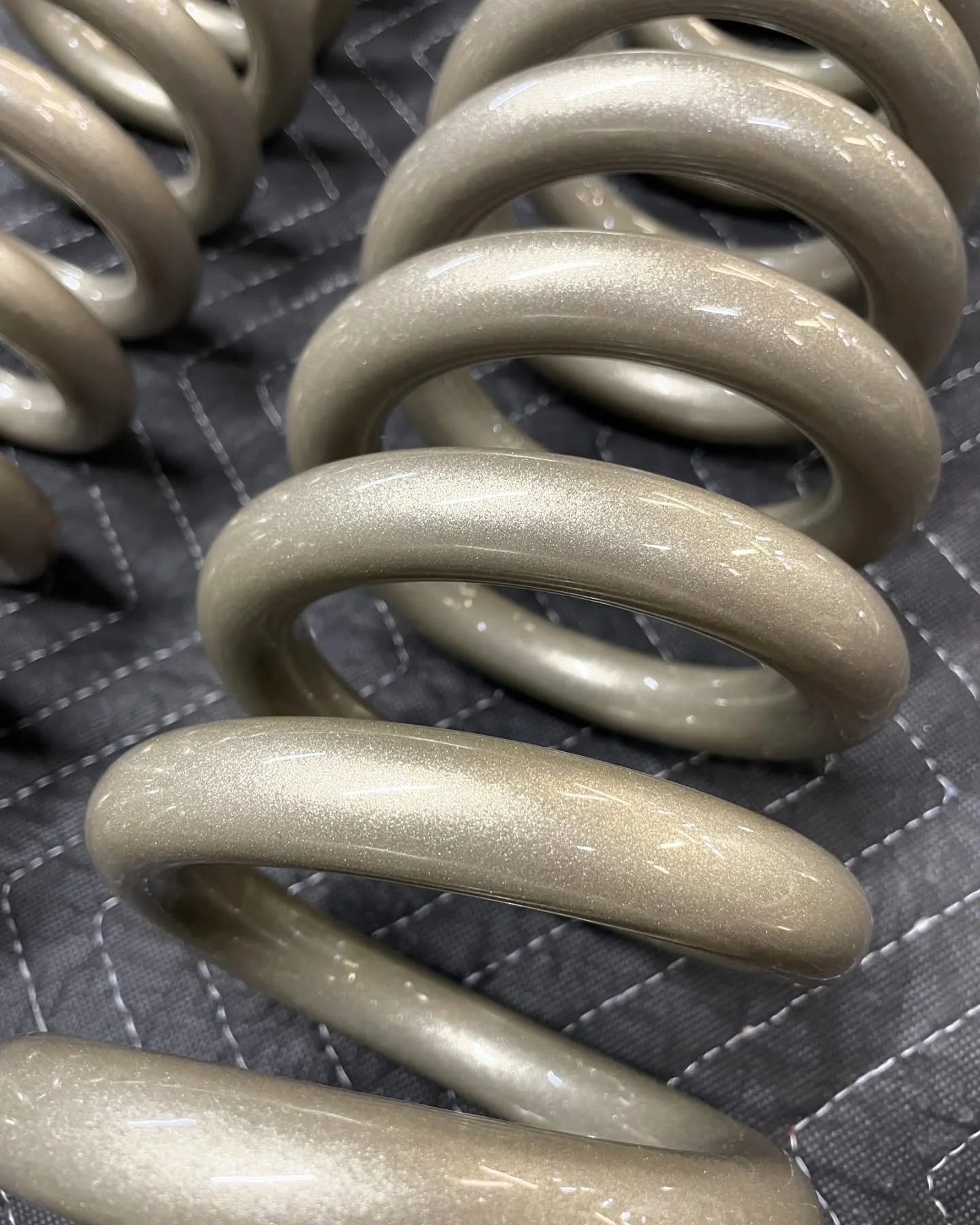 Close-up of beige, shiny, curved hair curlers arranged in a row on a black quilted surface.