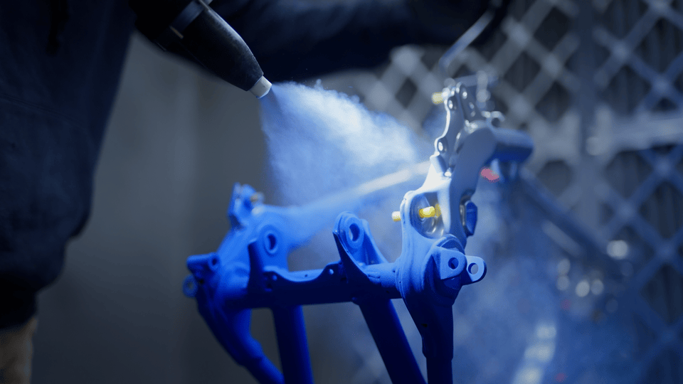 A person sprays blue paint onto a mechanical part in a factory or workshop setting.
