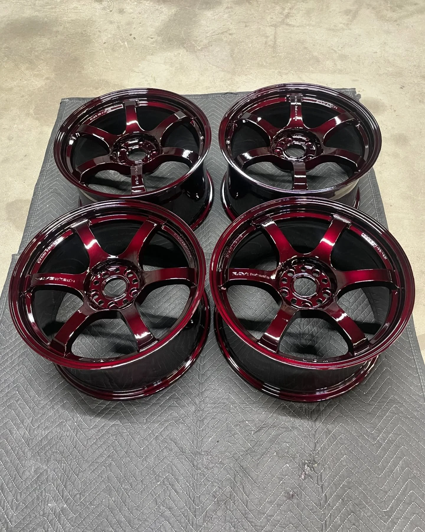 Four shiny red and black alloy wheels arranged on a padded surface, likely for a vehicle.
