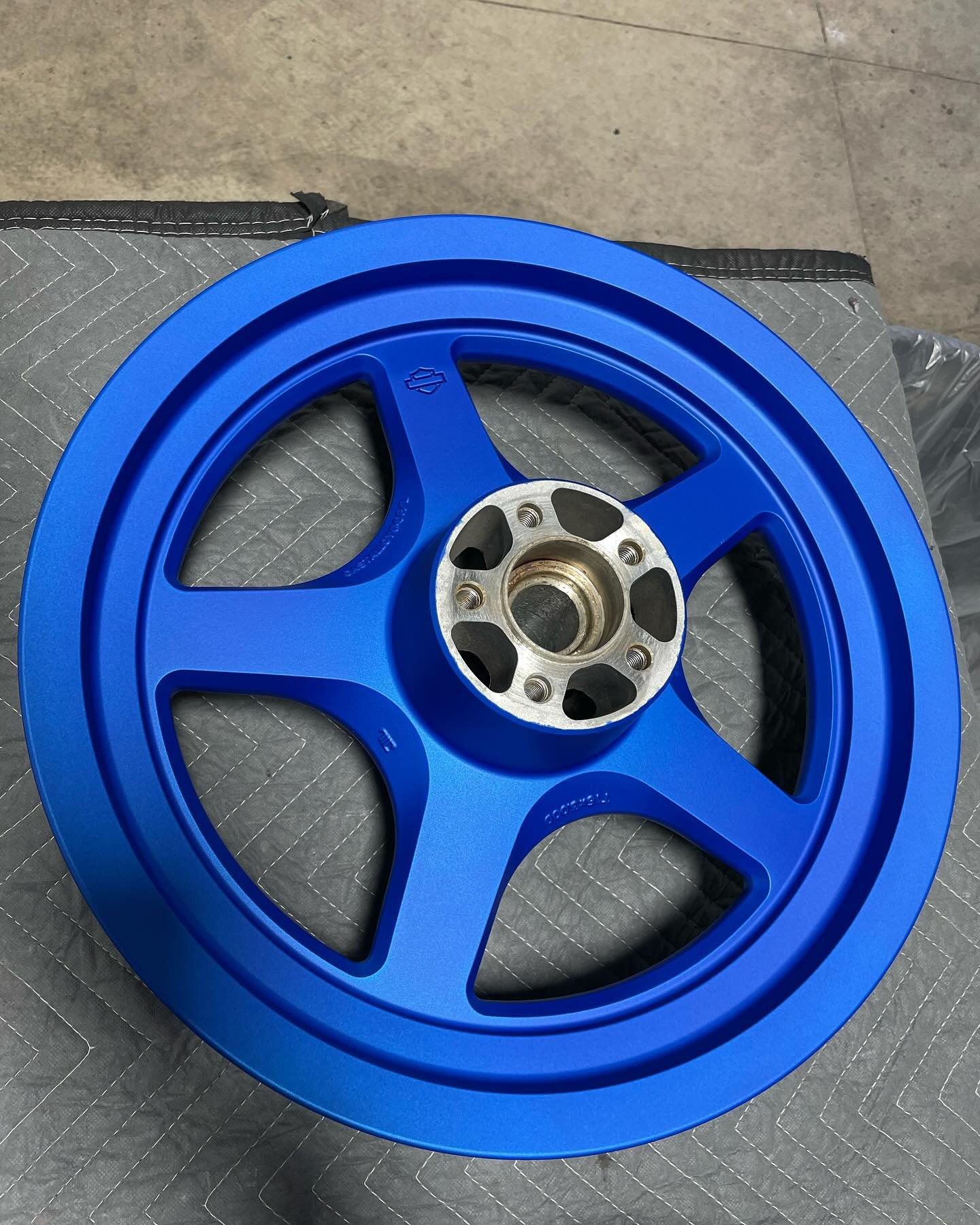 A blue motorcycle wheel with a metal hub, resting on a gray padded surface.