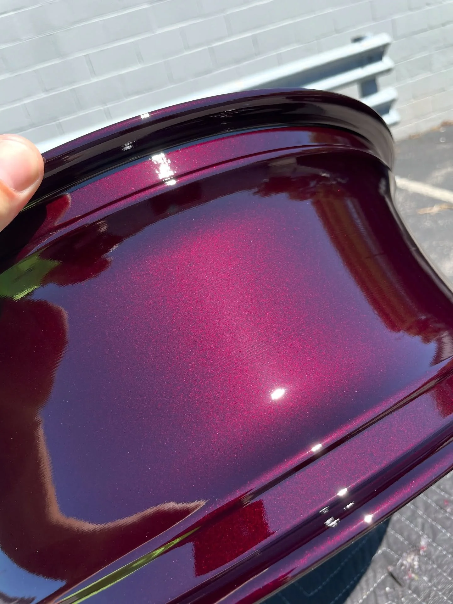 Close-up of a shiny, metallic, dark purple paint swatch with a glittery finish, reflecting sunlight.