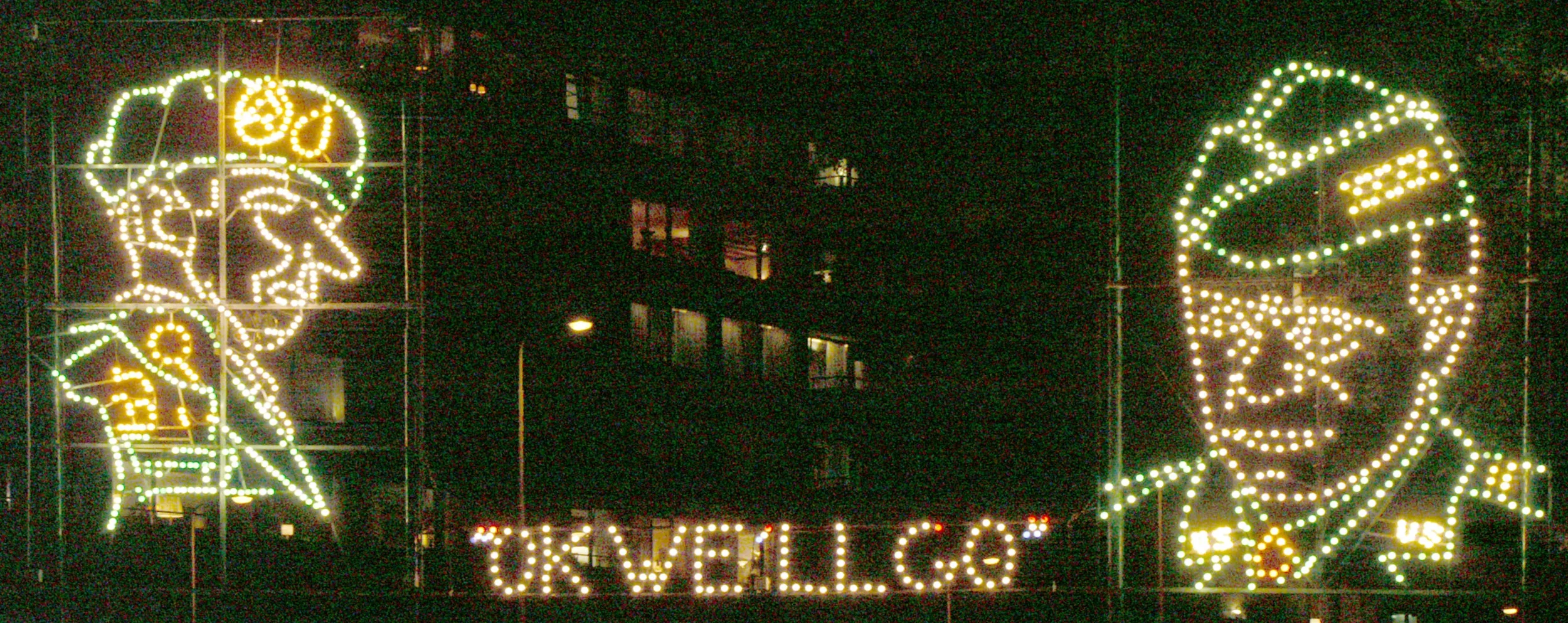 Nighttime holiday display featuring illuminated portraits of Santa Claus and President Joe Biden, with the words 'Stay Safe' and 'Take Care' and the phrase 'Our Well-Being' at the bottom.