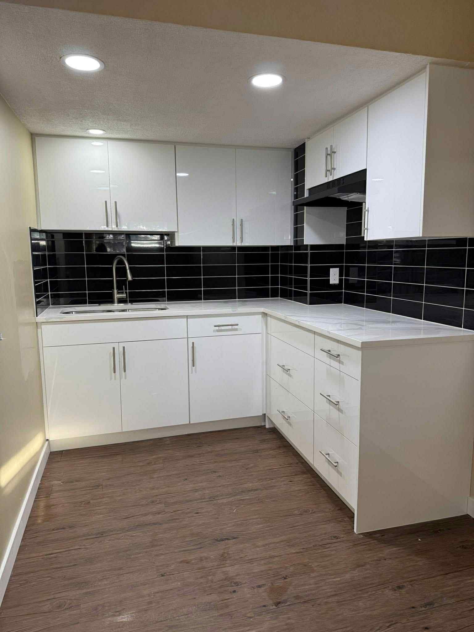 Modern kitchen with white cabinets, black tile backsplash, and wood-look flooring.