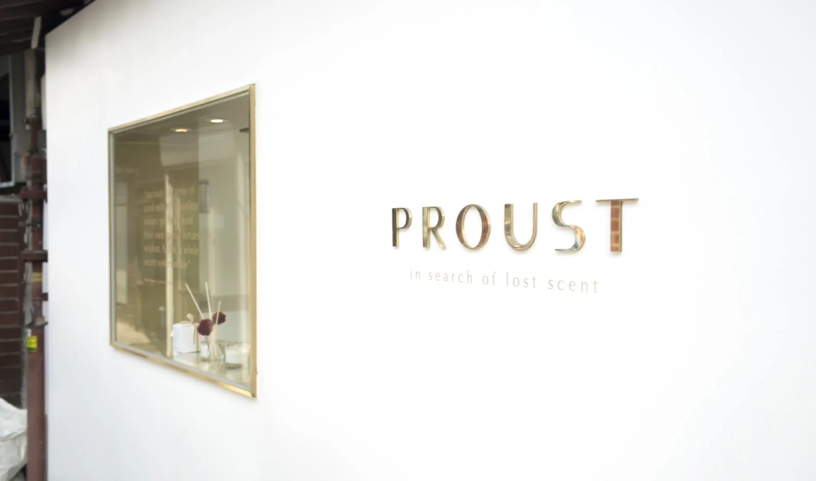 Proust logo on a white wall beside a brass-framed window