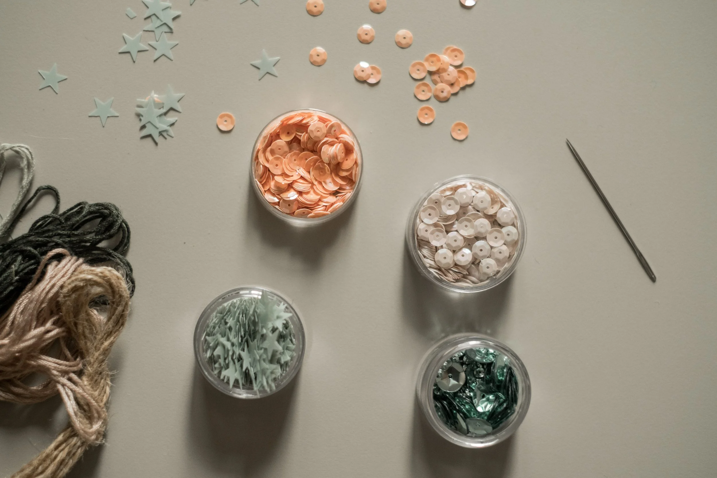 Varie decorazioni e materiali per craft su una superficie chiara, tra cui stelle e fiocchi di diverse forme e colori, fio di corda, aghi e altri ornamenti decorativi.