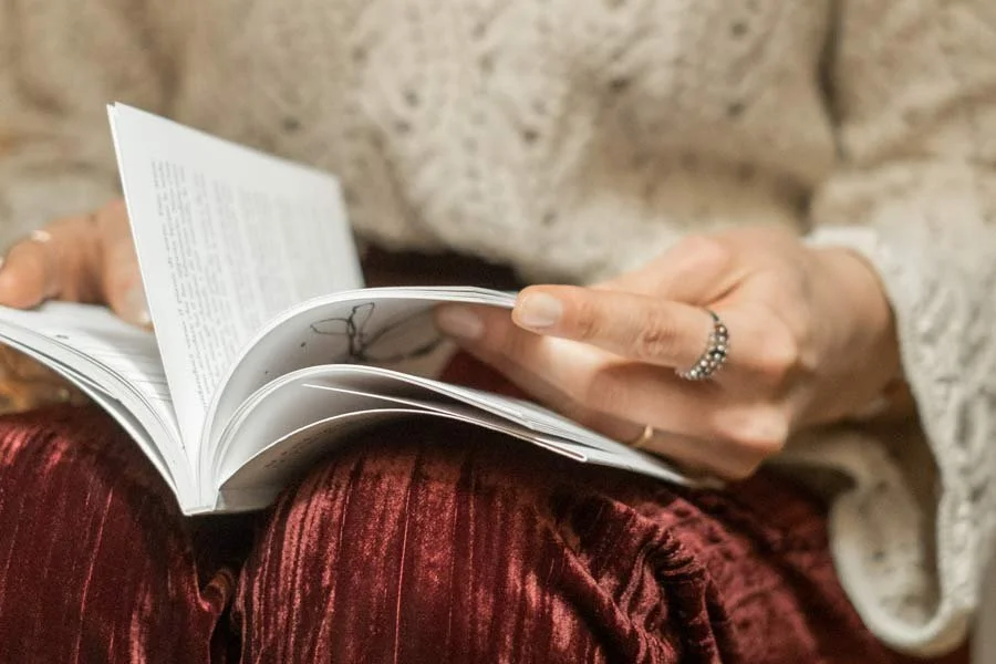 Una persona che legge un libro, mostrando le mani e parte del corpo, con indosso un anello e vestiti di velluto rosso.