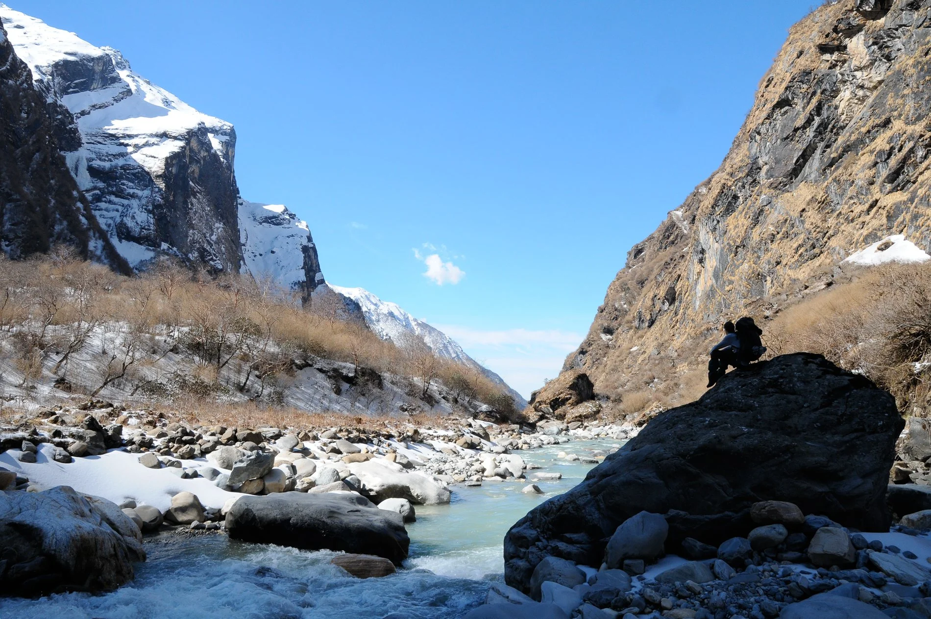 Rivière glacée au fond d'une gorge de montagnes rocheuses enneigées, que contemple Simon Tossens, assis sur un rocher surplombant le paysage.