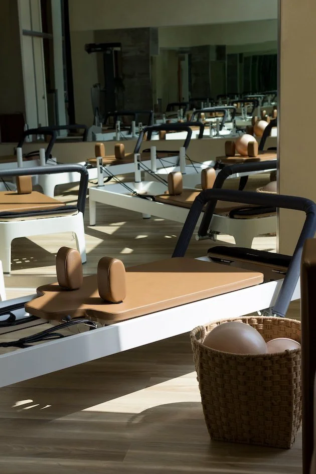 Row of Pilates reformer machines in a fitness studio, with a basket of exercise balls nearby.