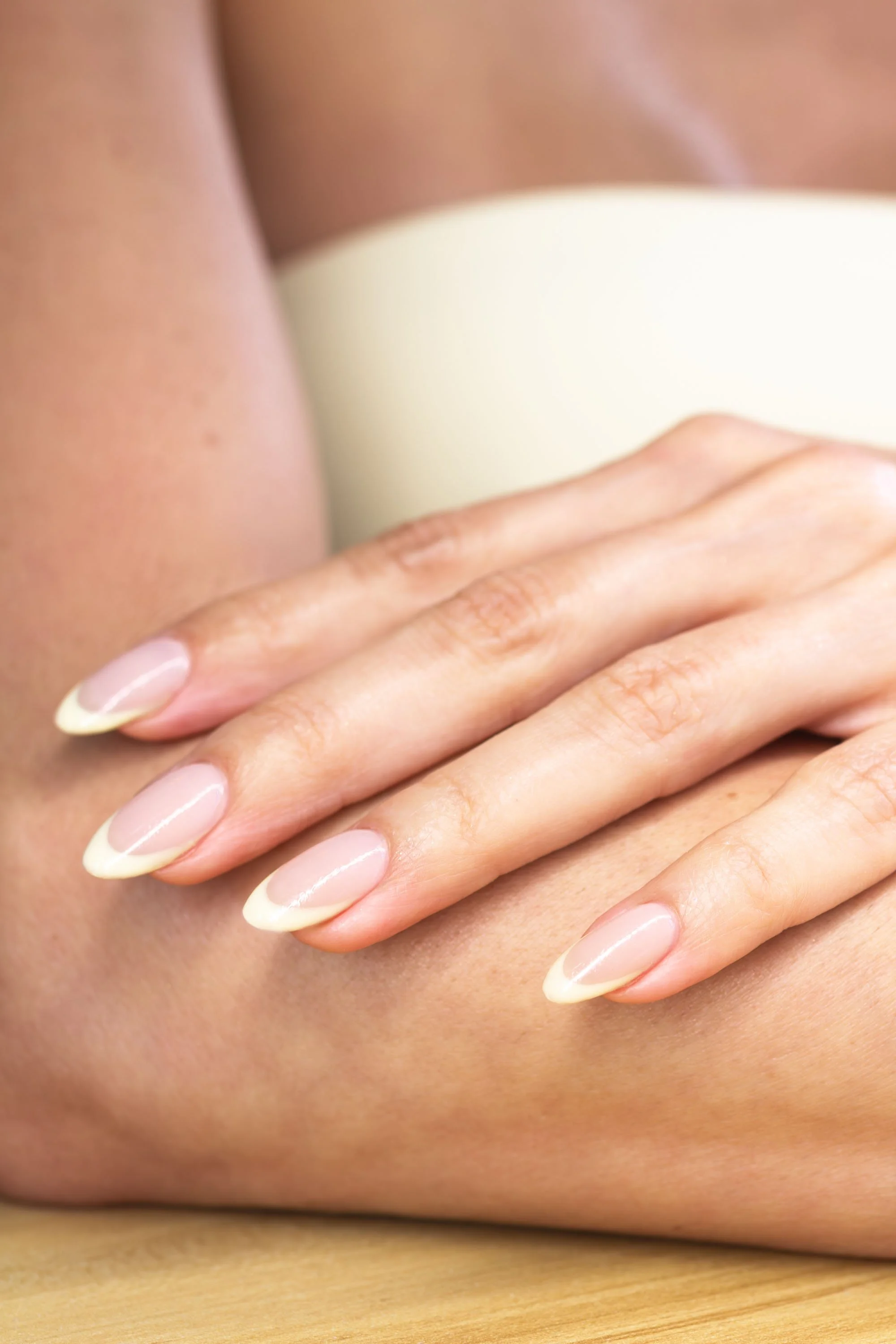 Close-up of a hand with manicured nails resting on an arm with a yellow backdrop.