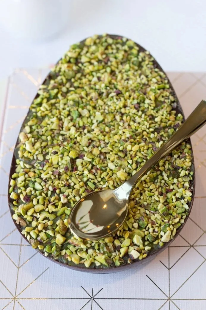 Oval dish filled with chopped pistachios, with a metal spoon resting on top.