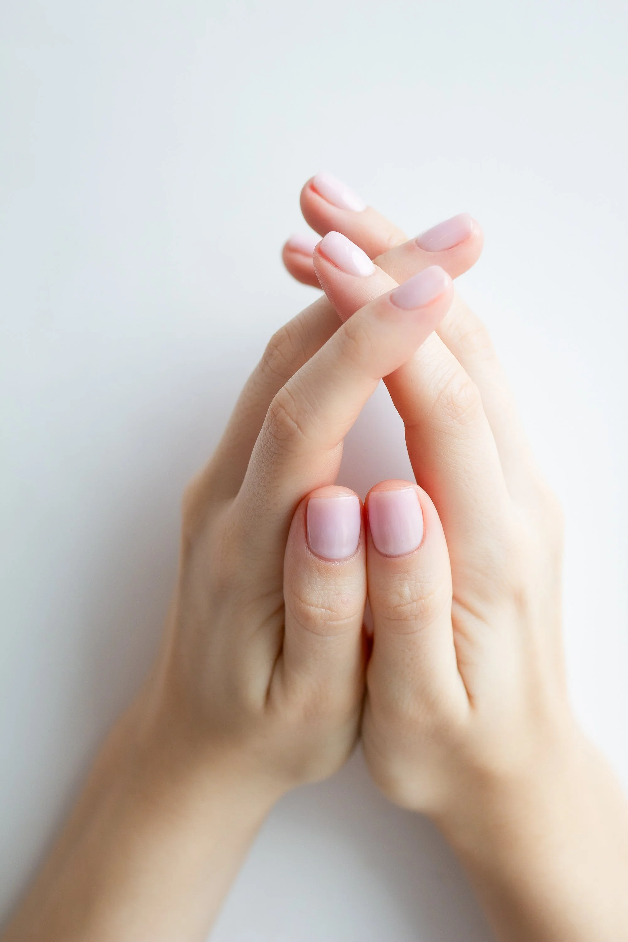 Close-up of two hands with neatly manicured nails clasped together against a plain white background.