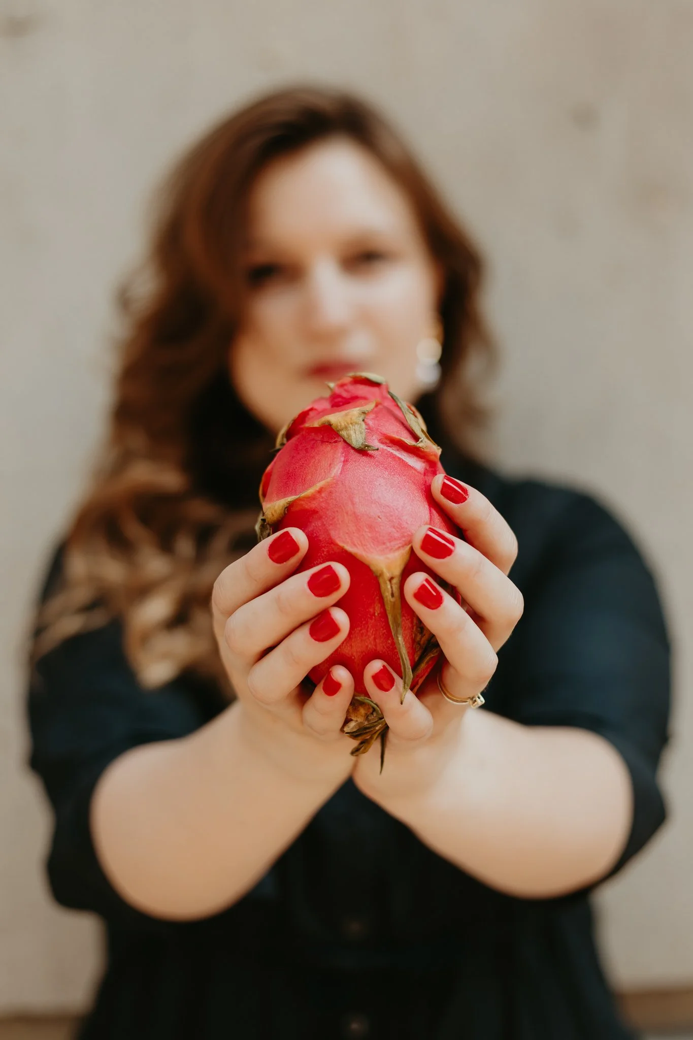 A woman with dark skin and curly black hair is holding a sandwich with meat, vegetables, and cilantro. She appears to be licking her finger and enjoying the food.