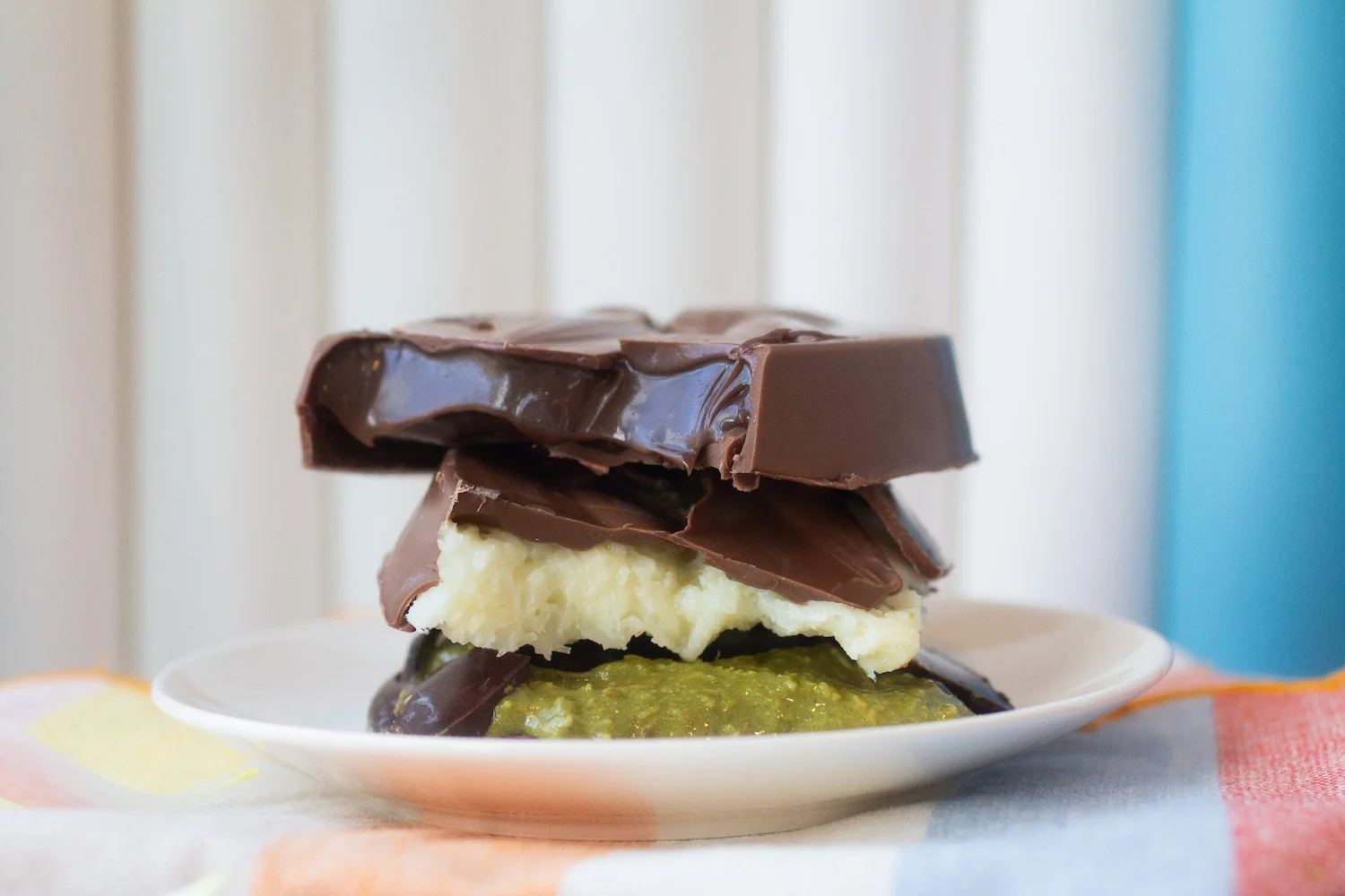 Stacked chocolate and vanilla ice cream with green sauce on a white plate, with a blurred background of a blue and white wall.