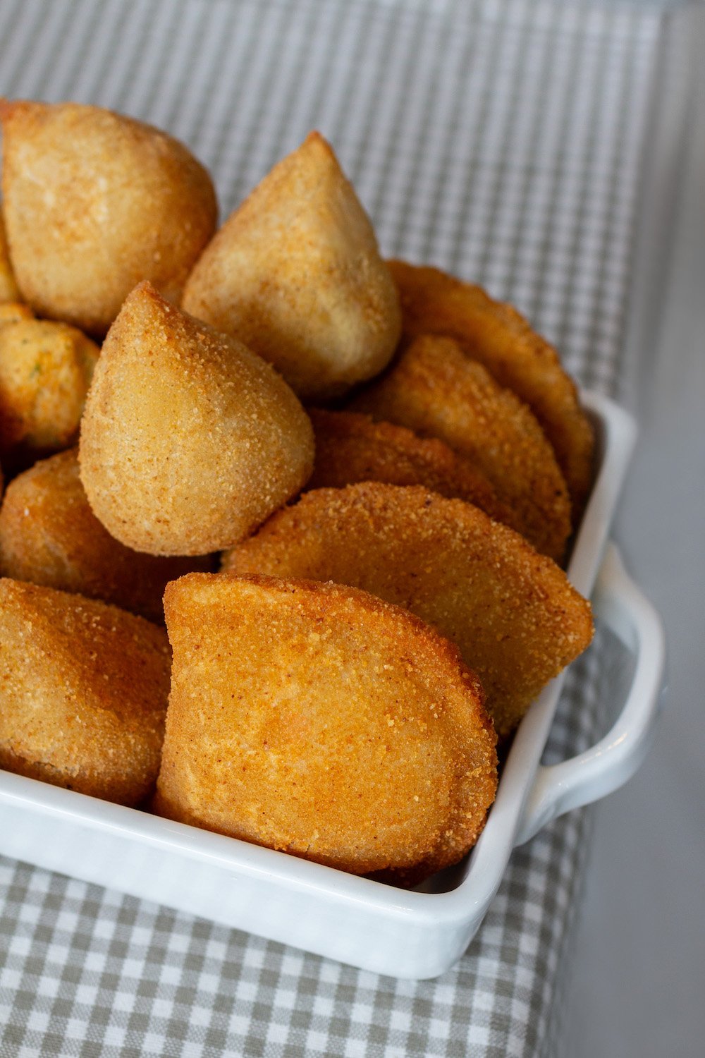 A white square dish filled with golden fried hush puppies, resting on a gray and white checkered cloth.