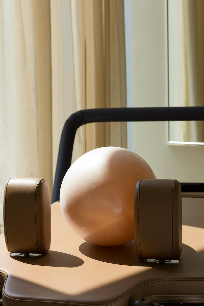 A beige sphere and two brown speakers on a brown cushioned surface against a backdrop of cream curtains and a window.