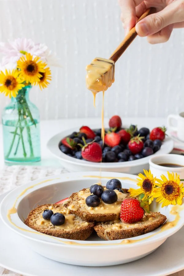 Peach and strawberry toast topped with blueberries, drizzled with honey, served with a bowl of mixed berries and a cup of coffee, decorated with yellow sunflowers.