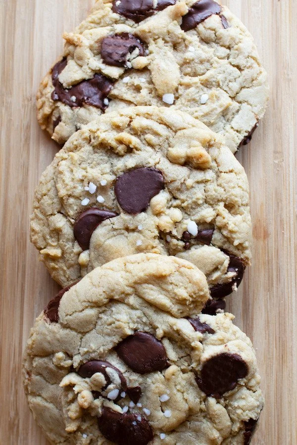 Three chocolate chip cookies on a wooden surface.