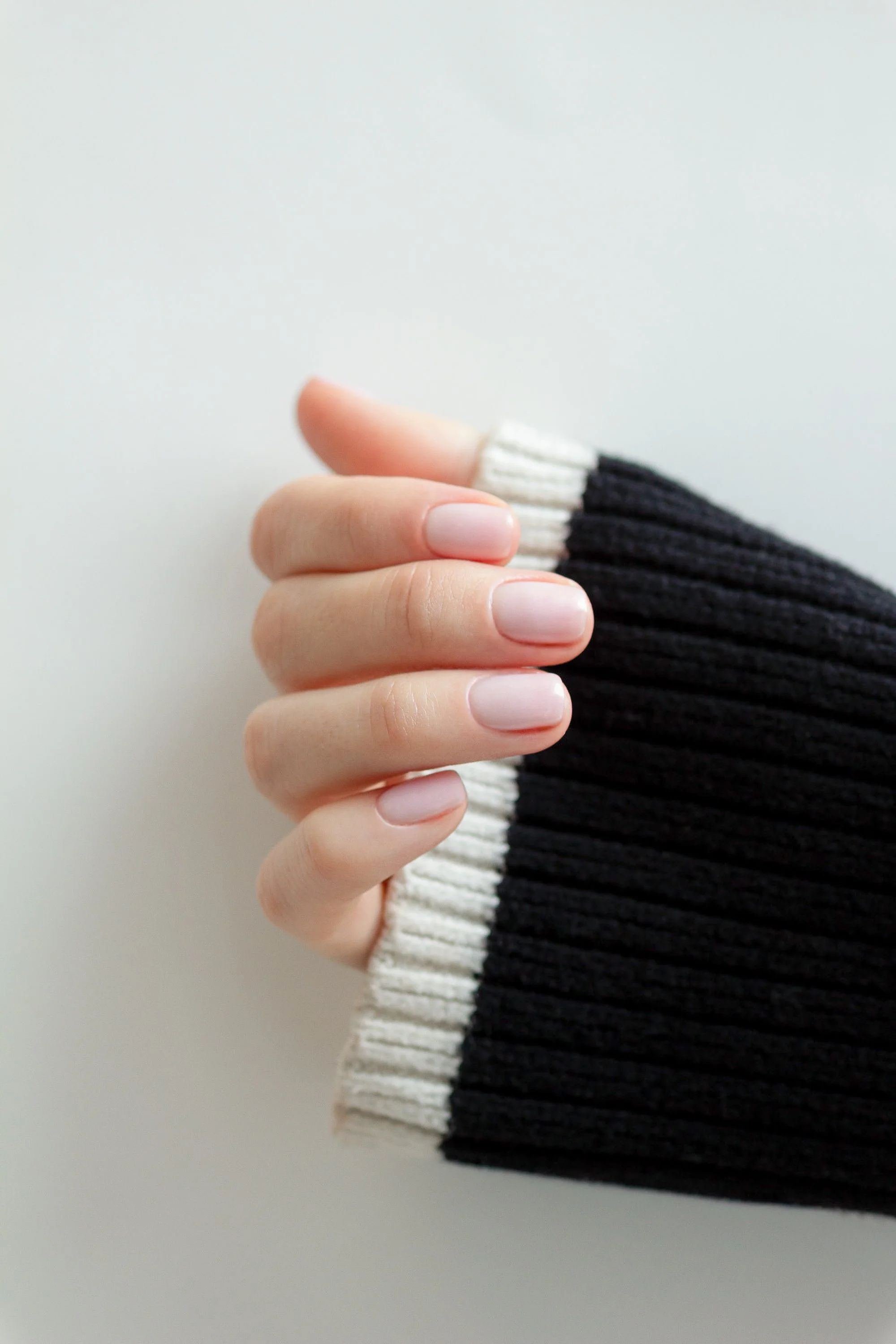 Close-up of a hand with natural nails, wearing a black and white striped ribbed sweater, against a plain background.