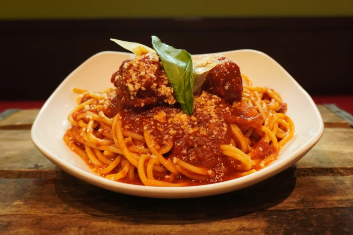 Plate of spaghetti with meatballs topped with tomato sauce, cheese, and a basil leaf