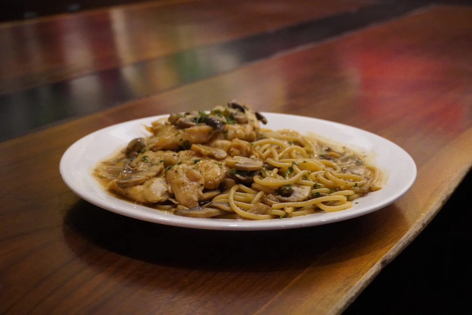 Plate of spaghetti with chicken and mushrooms in a sauce on a wooden table.