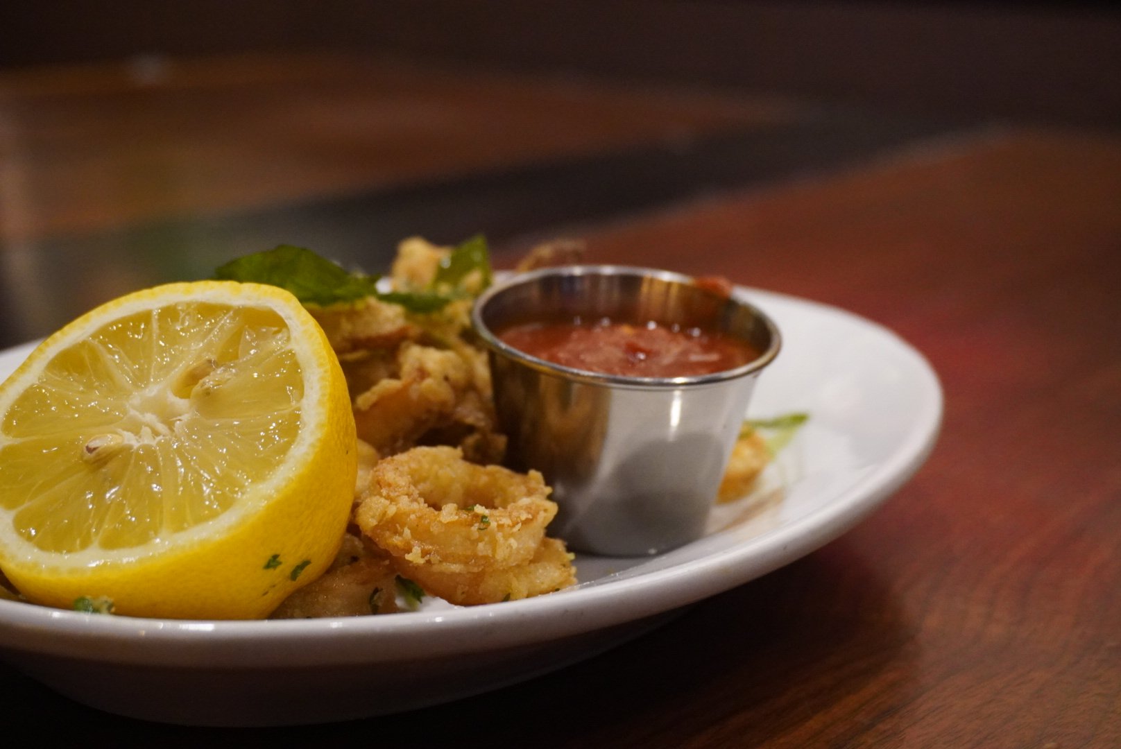 Fried calamari with lemon wedge and dipping sauce on a white plate.