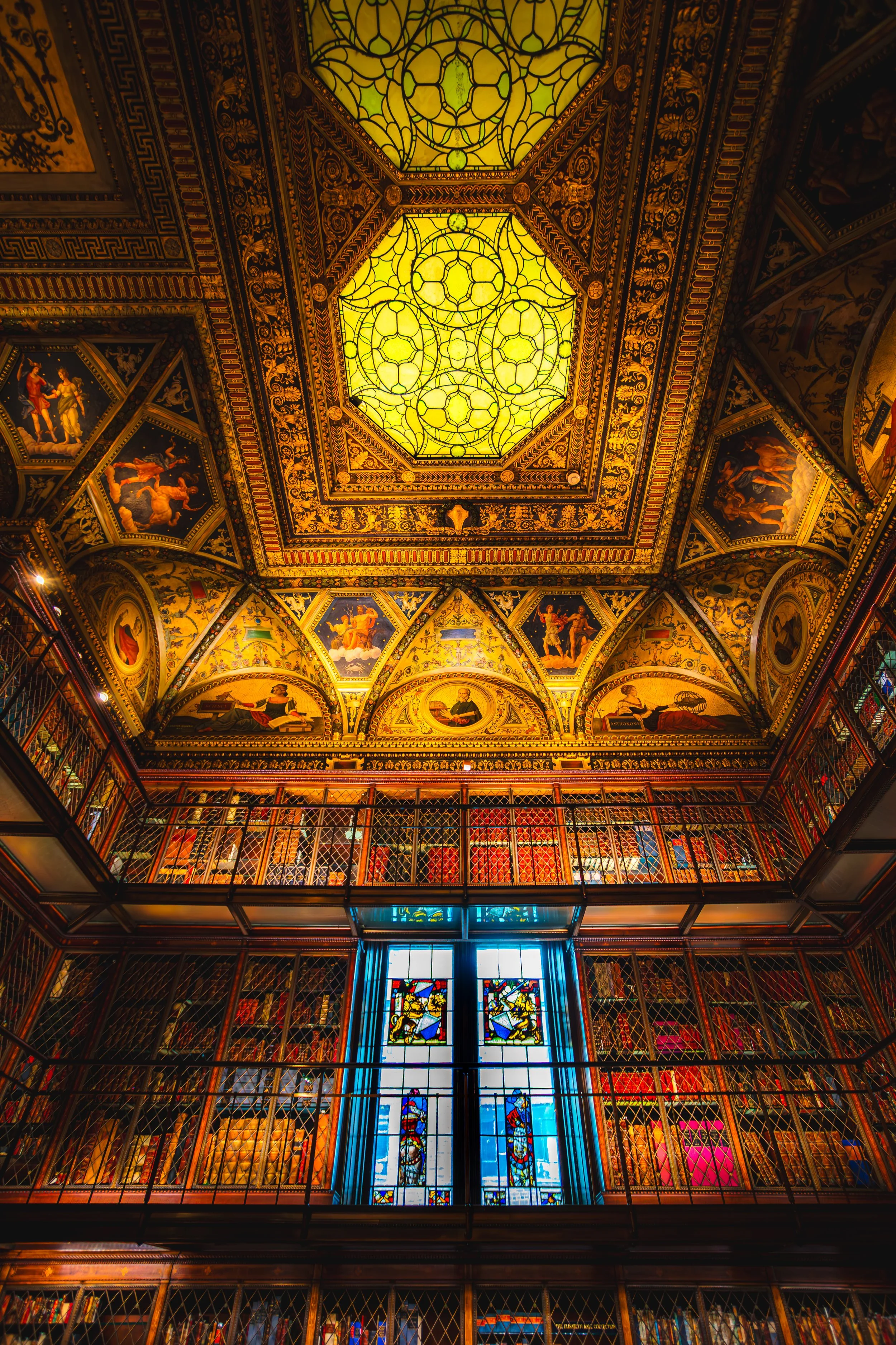 Interior view of the JP Morgan historic library with ornate gold and colorful artwork ceilings, stained glass windows, and multiple bookshelves on multiple levels.