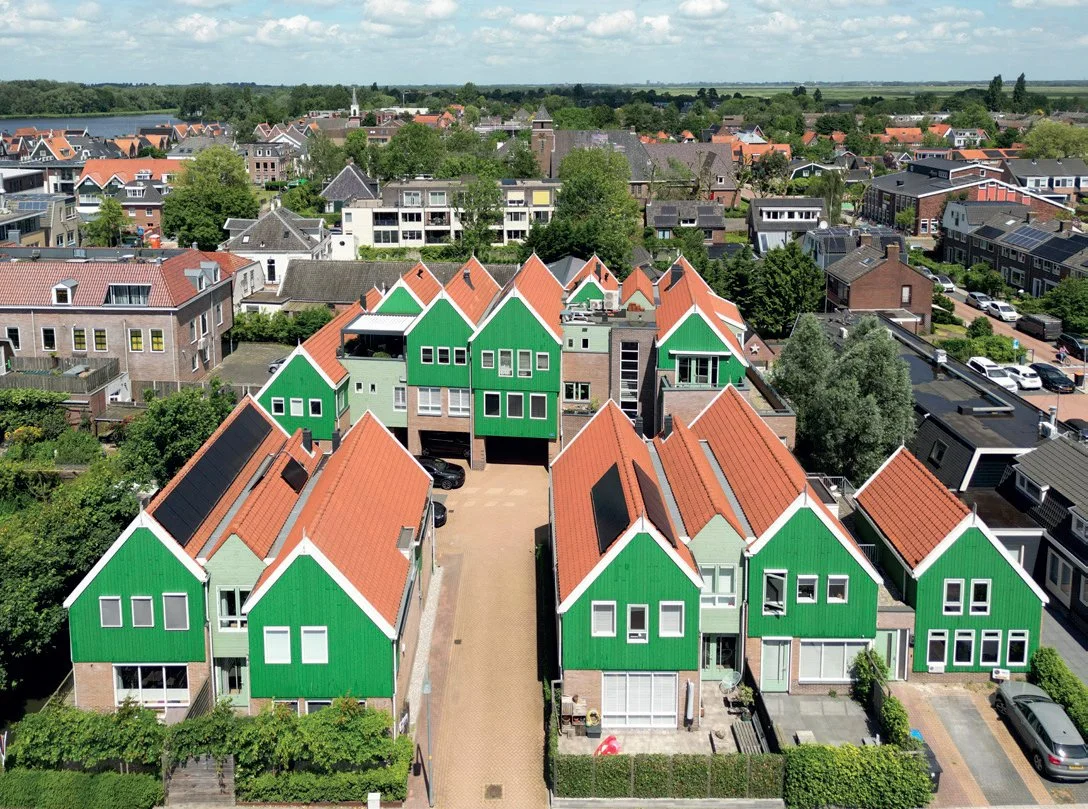 Luchtfoto van een woonwijk met huizen die groene gevels en rode daken hebben, omgeven door groen en bomen.