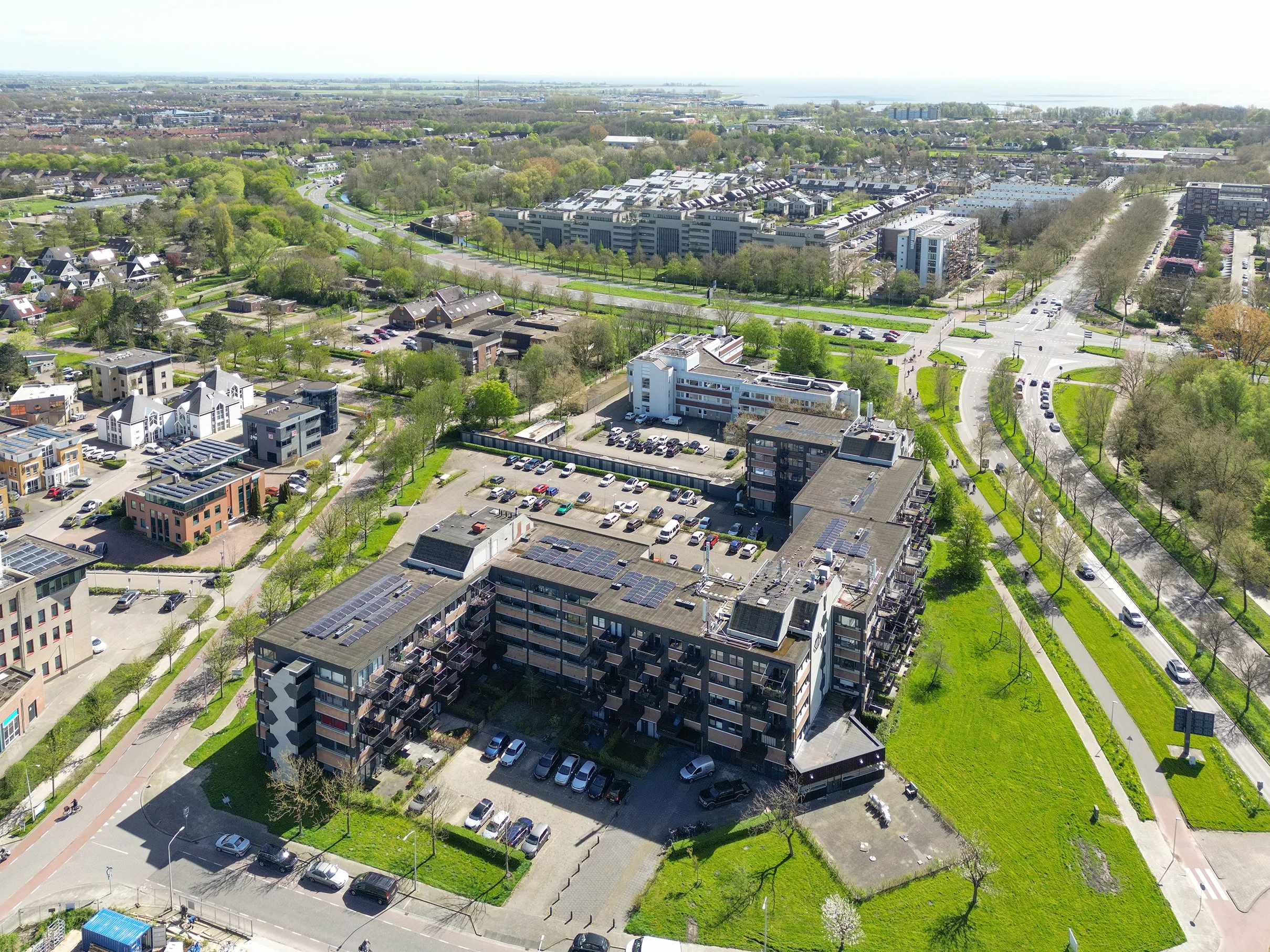 Luchtfoto van een woonwijk met verschillende huizen, appartementen en groene straten, nabij een meer en open velden in de achtergrond.