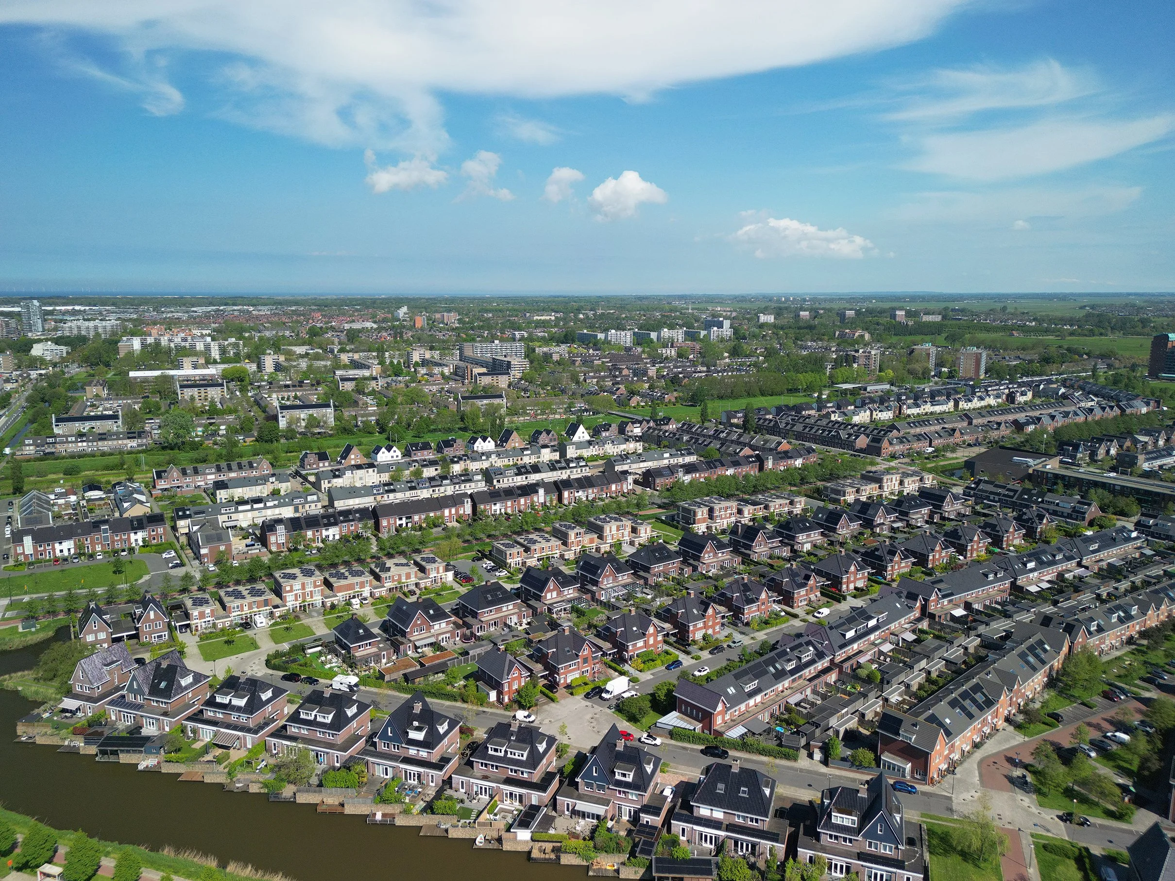 Luchtfoto van een woonwijk met huizen, straten en veel groen, en een uitgestrekte lucht met enkele wolken.
