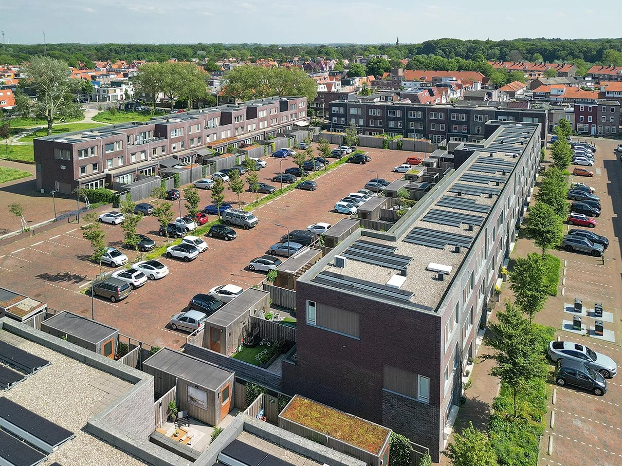 Uitzicht op een woonwijk met appartementen, parkeerplaatsen en groene bomen.